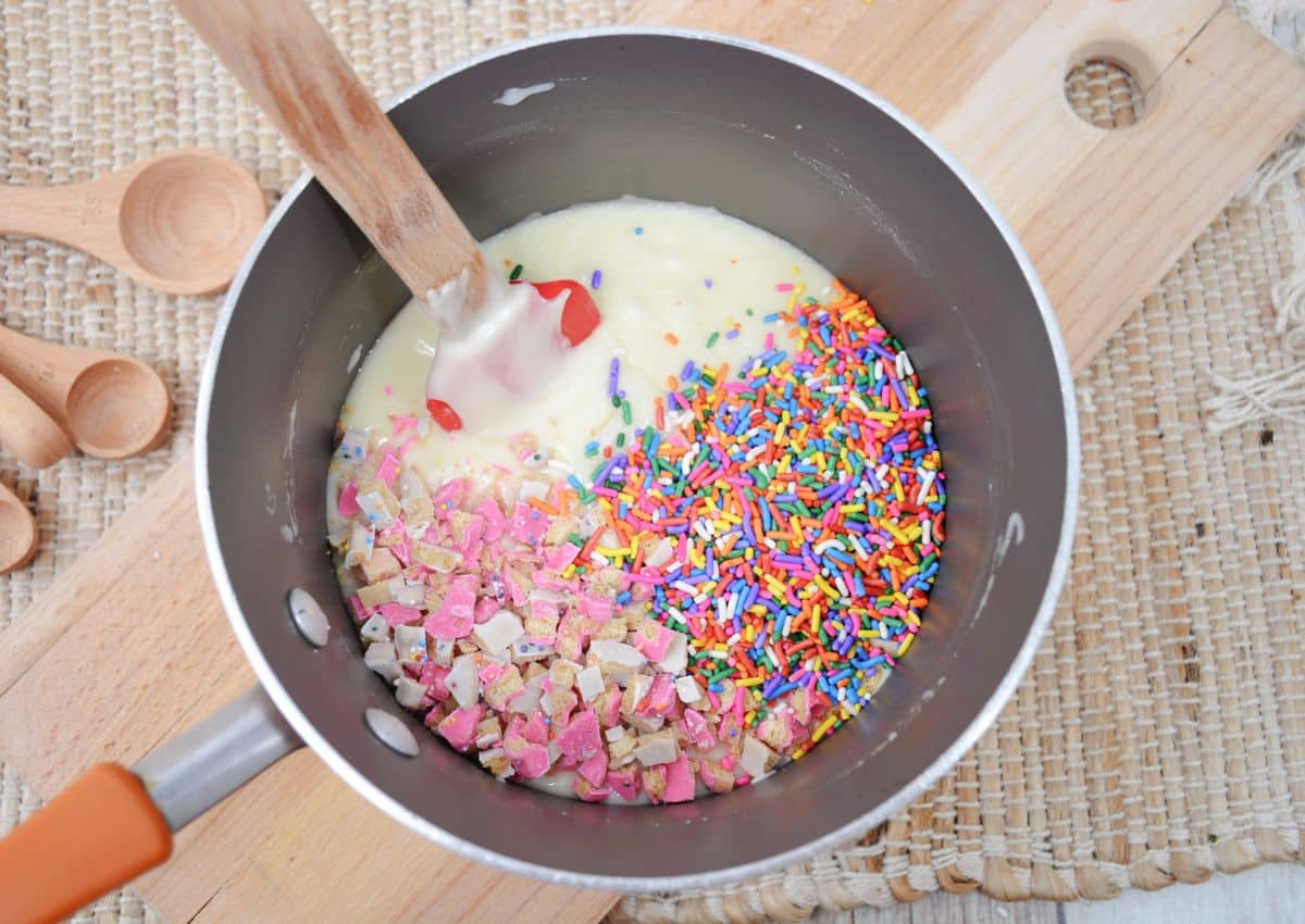 melted white chocolate, sprinkles, and cookie pieces being mixed together in a large saucepan.
