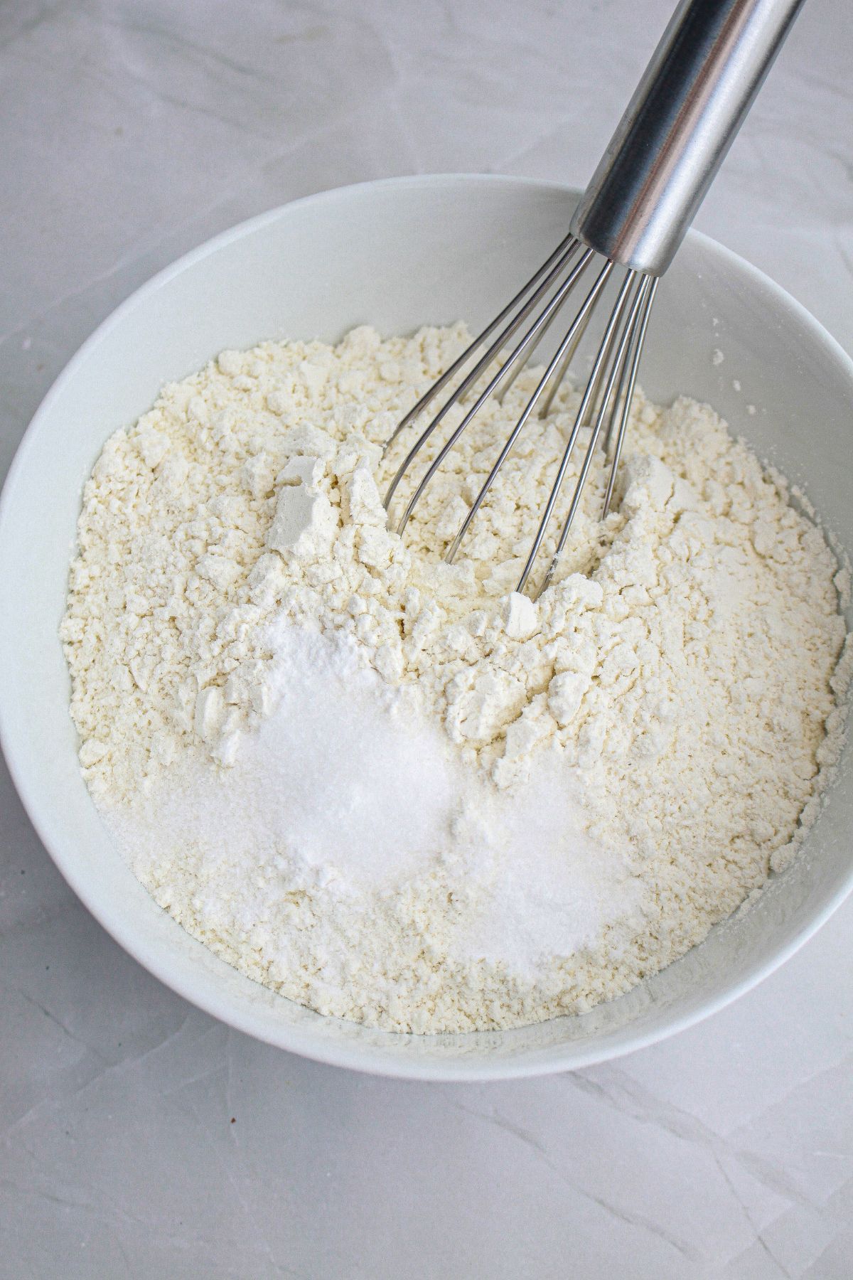 flour, sugar, salt, and baking powder being mixed in a bowl with a whisk.