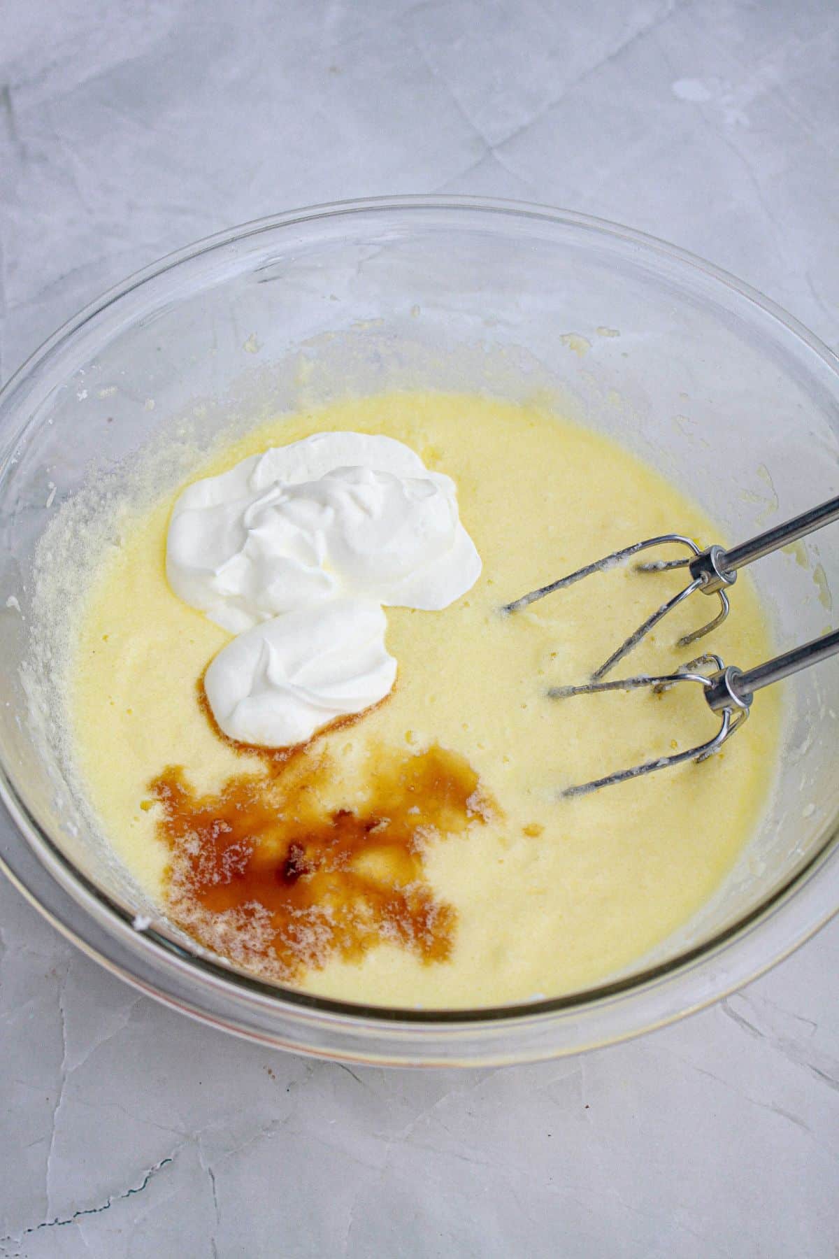 sour cream and vanilla extract being added to batter in a glass bowl.
