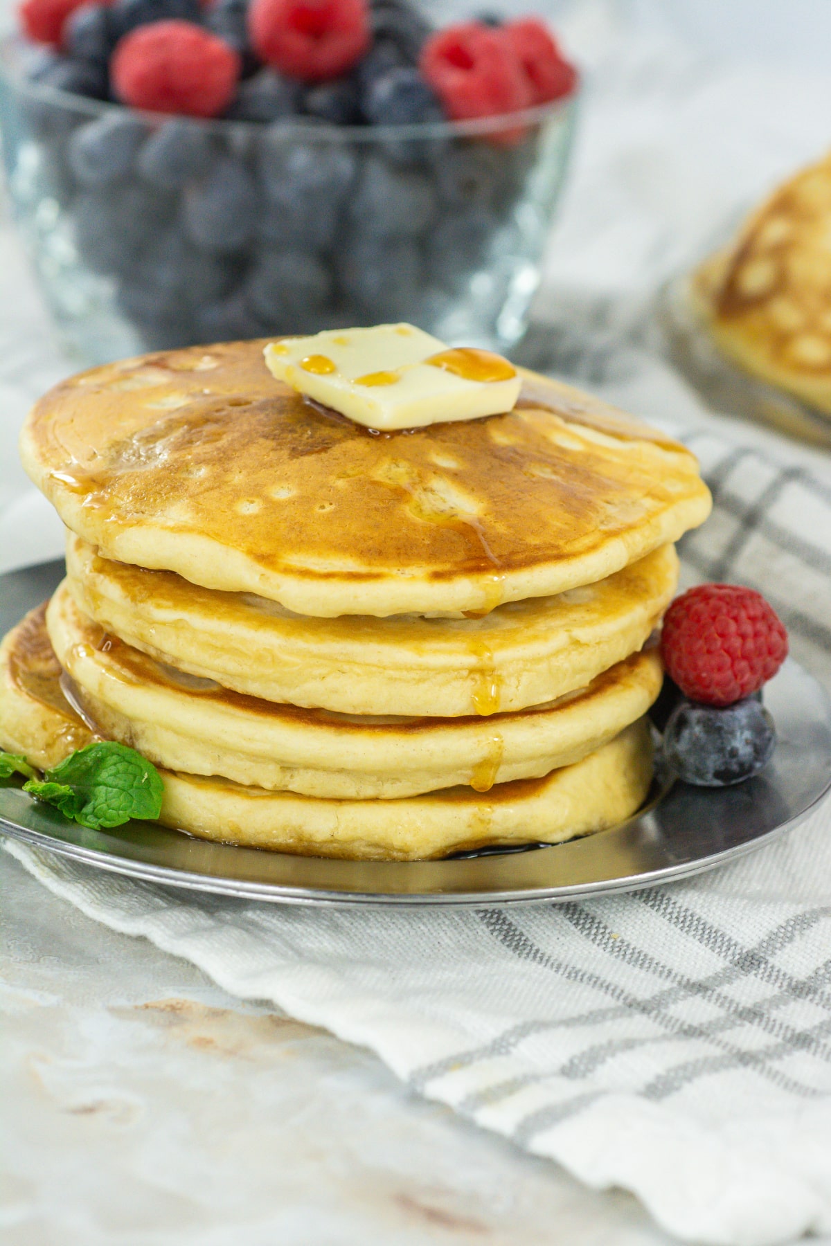 four pancakes on a plate topped with a pat of butter, and syrup.