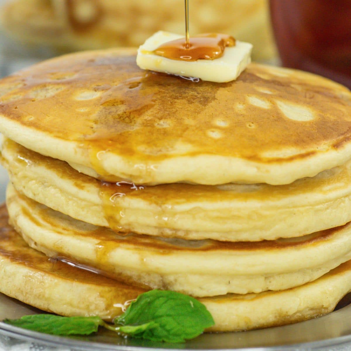 four pancakes on a plate topped with a pat of butter, and syrup.