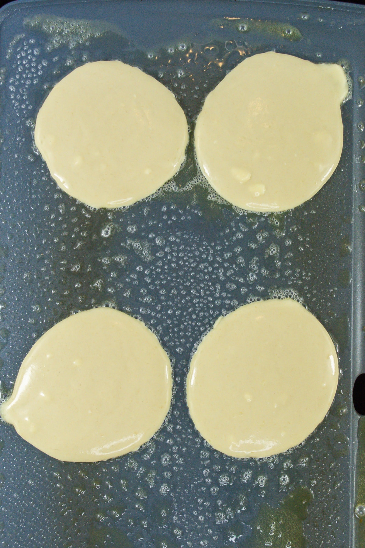 four pancakes being cooked on a buttered griddle.