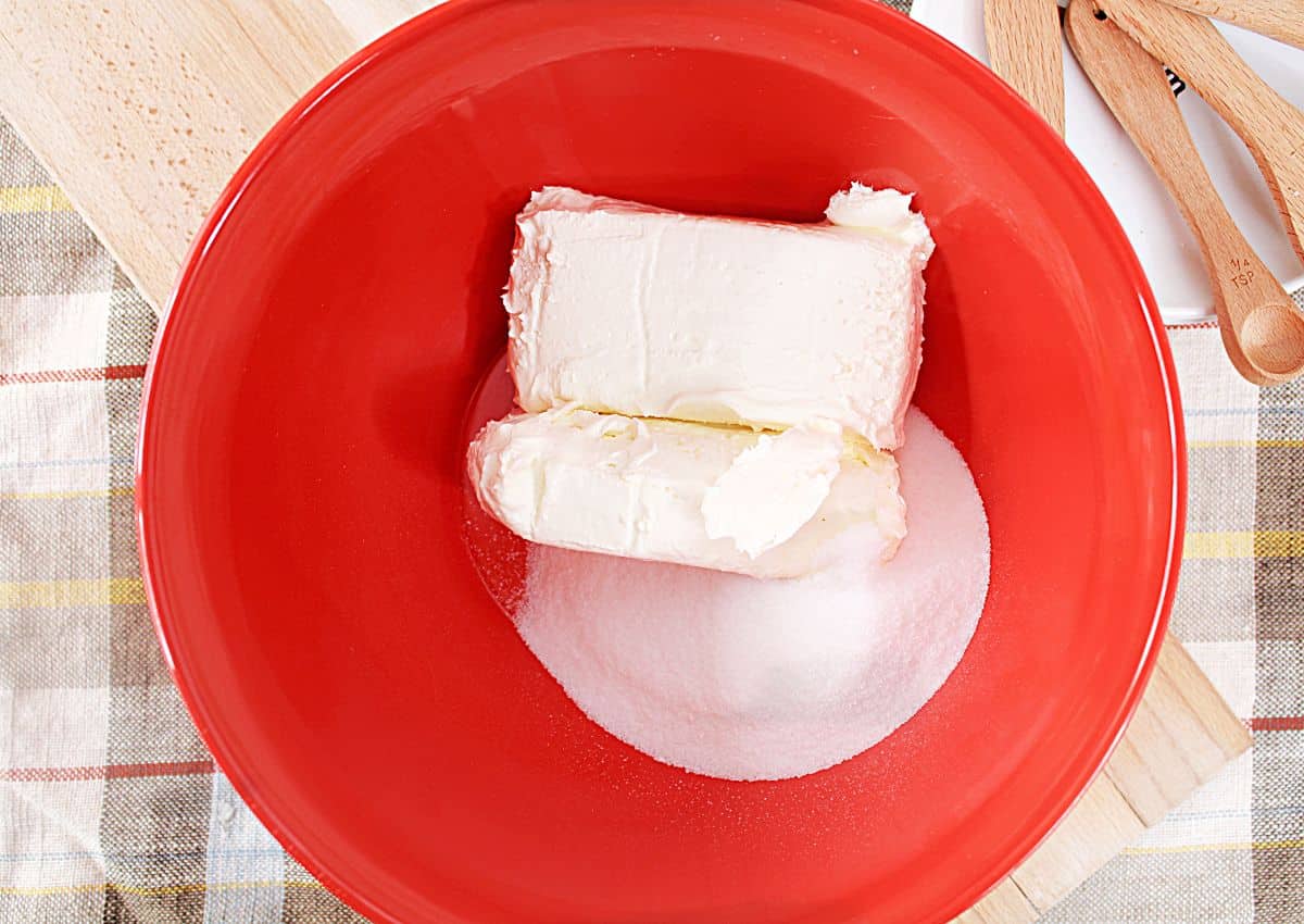 cream cheese and sugar being mixed together in large mixing bowl.