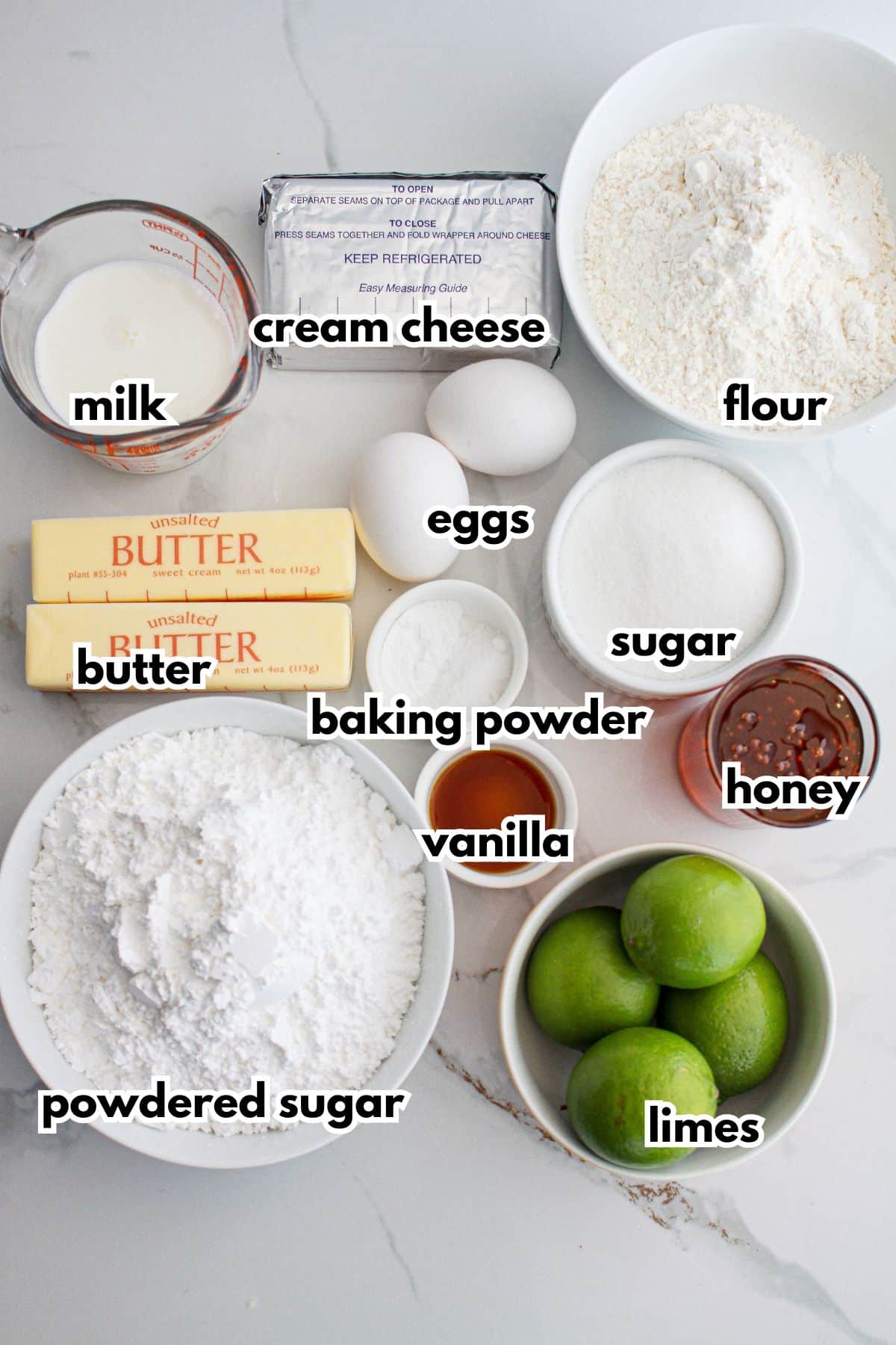 bowls of milk, cream cheese, flour, eggs, butter, baking powder, sugar, powdered sugar, limes, vanilla, and honey.