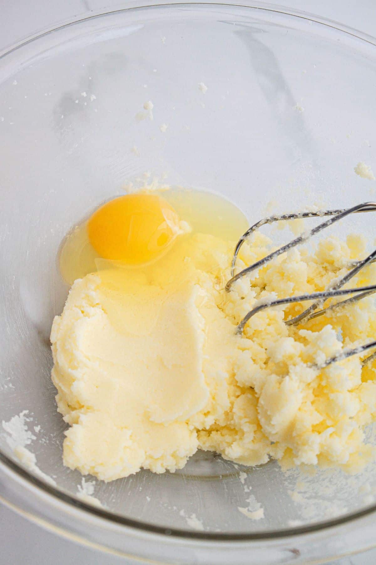butter, sugar and eggs being mixed together in a glass bowl.