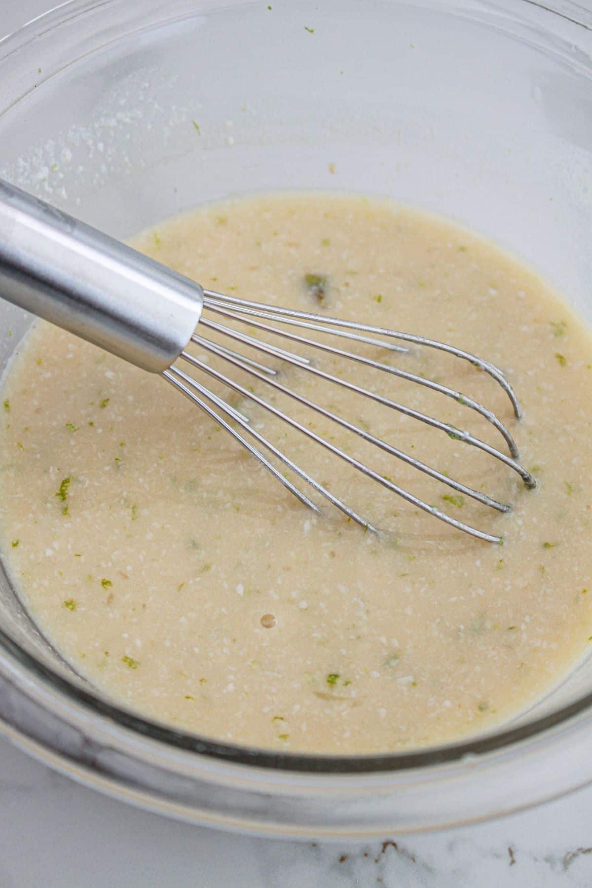 wet ingredients being mixed in a glass mixing bowl.