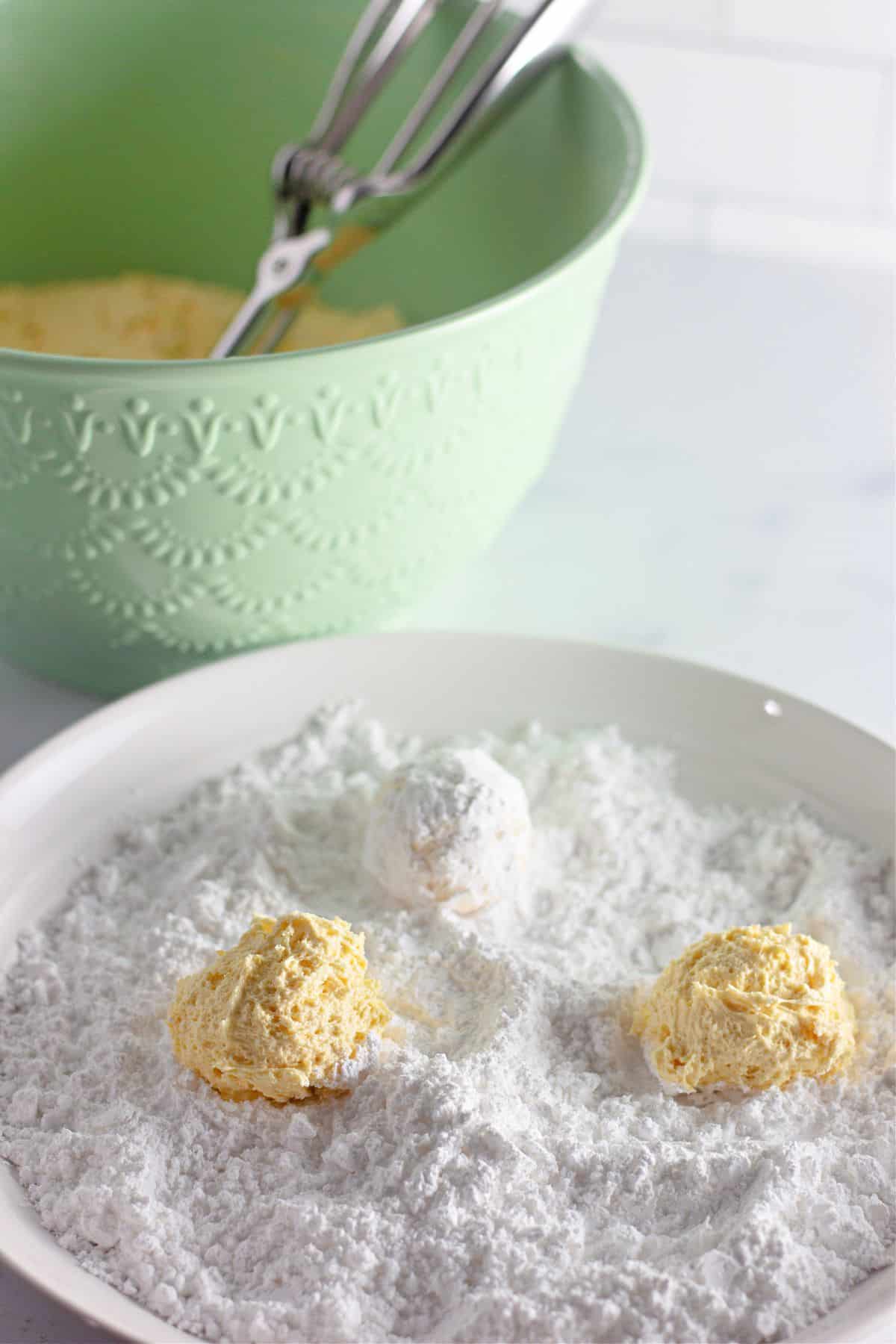 dough balls being rolled in a rolled powdered sugar on a small plate.