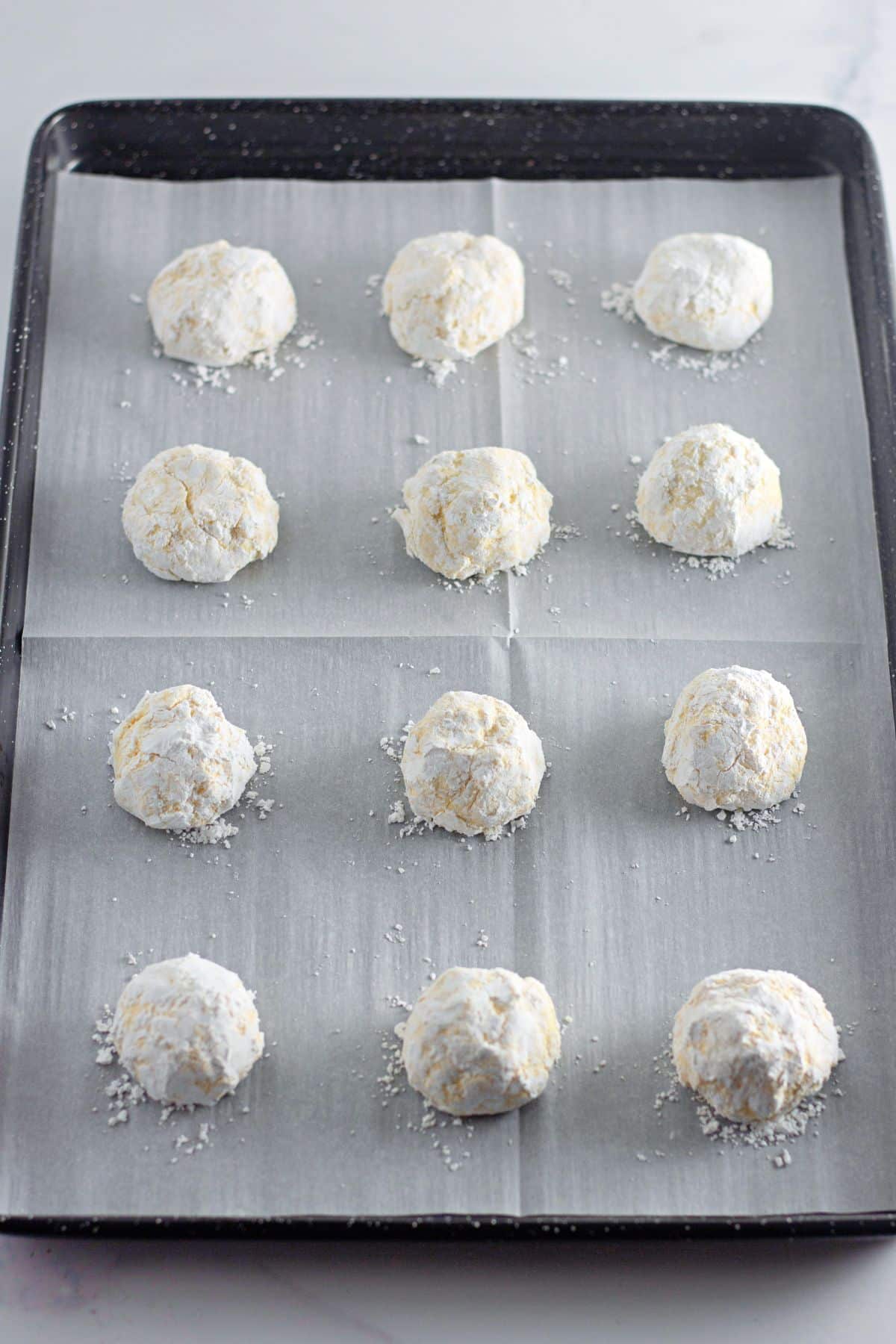cookie dough balls rolled in powdered sugar on a baking sheet.