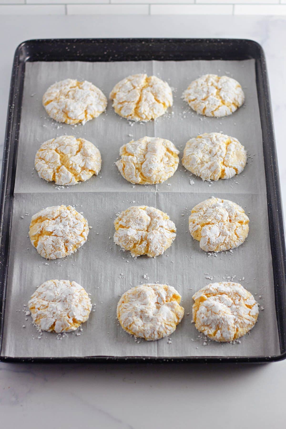 lemon cool whip cookies cooling on a parchment lined baking sheet.