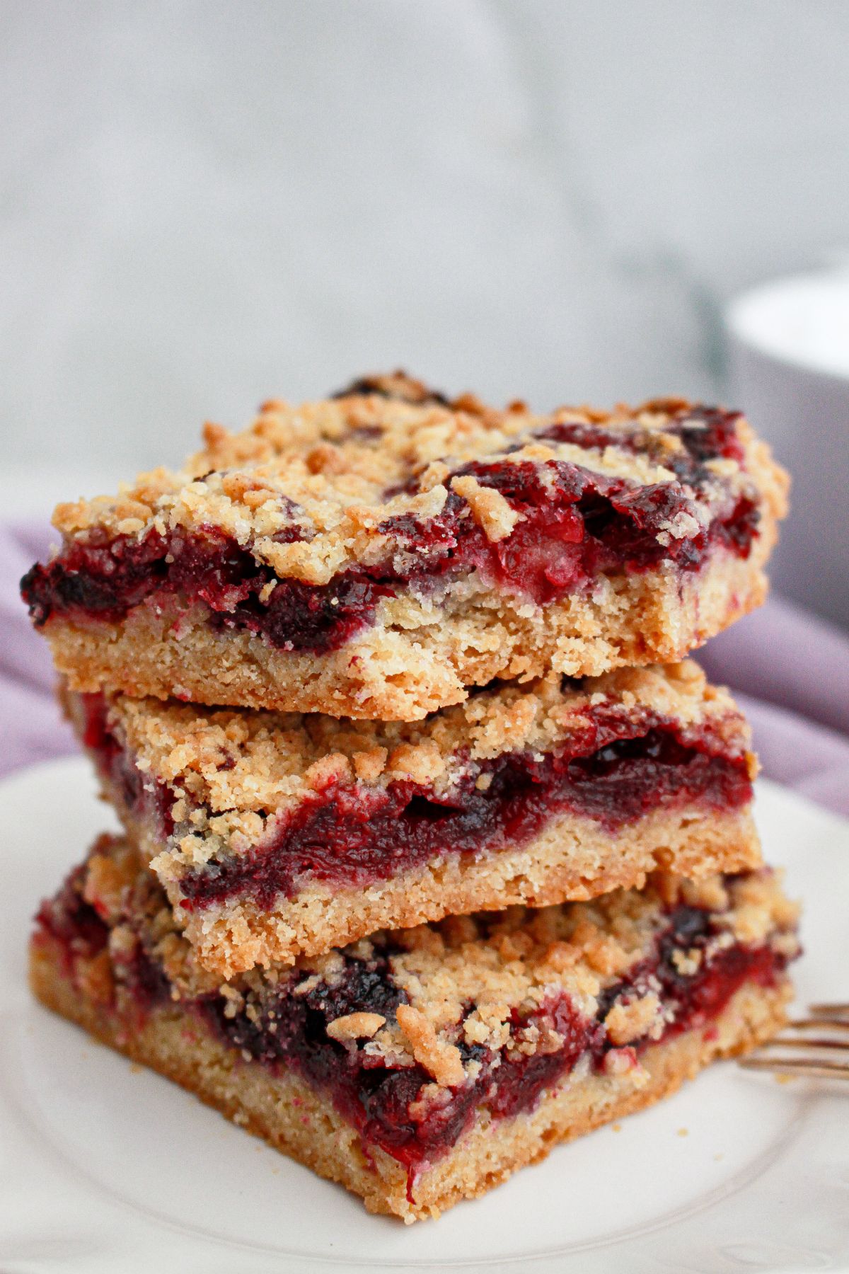 three lemon raspberry crumble bars stacked on a plate.