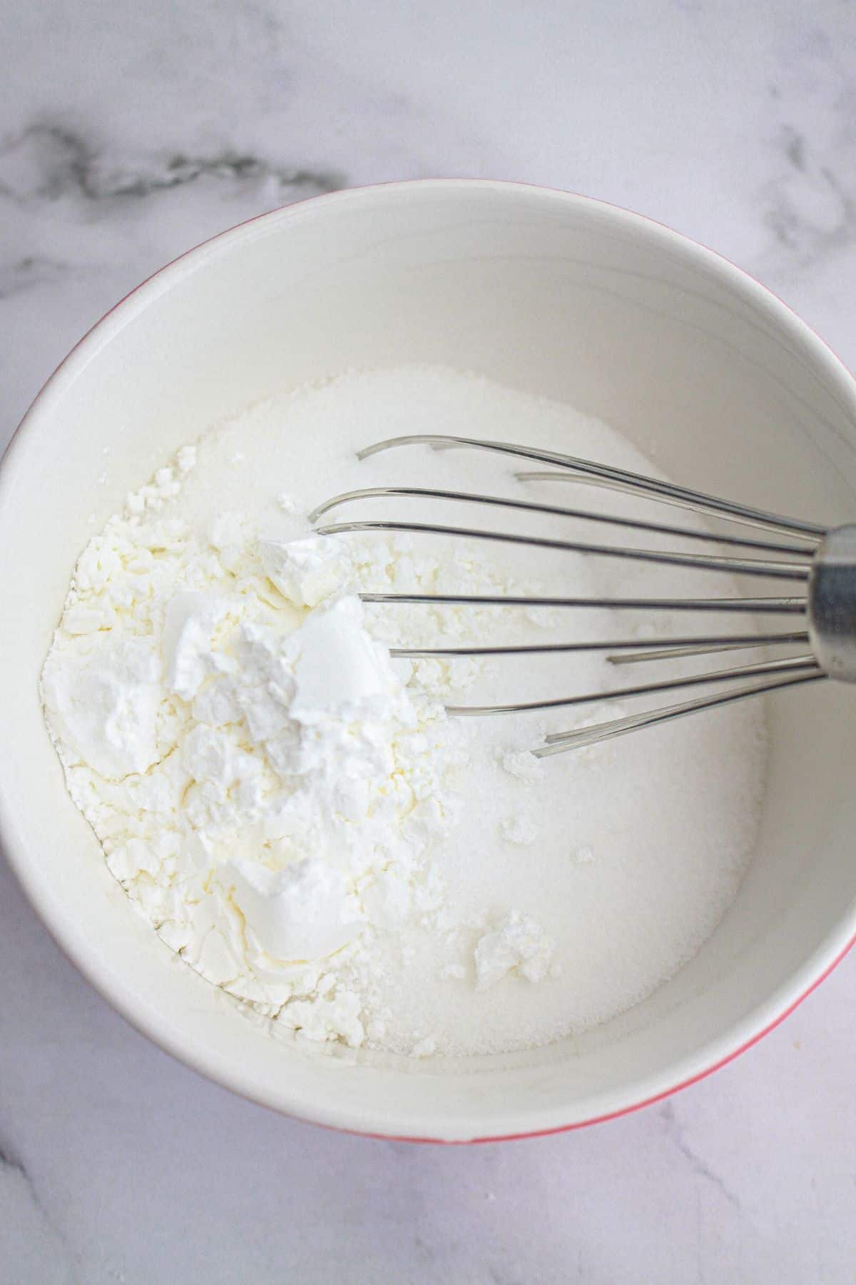 sugar and cornstarch being mixed with a whisk in a mixing bowl.