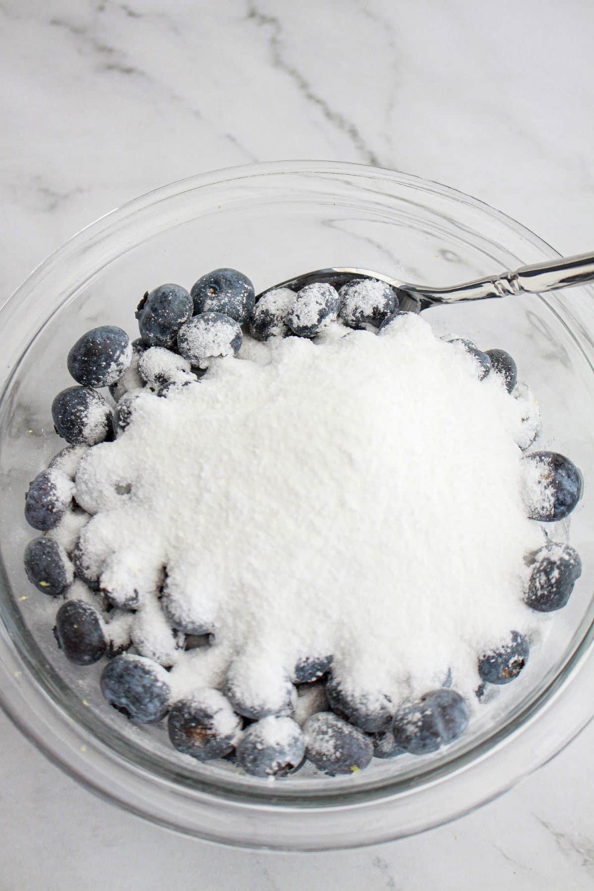 blueberries, sugar, and cornstarch being mixed in a glass mixing bowl.