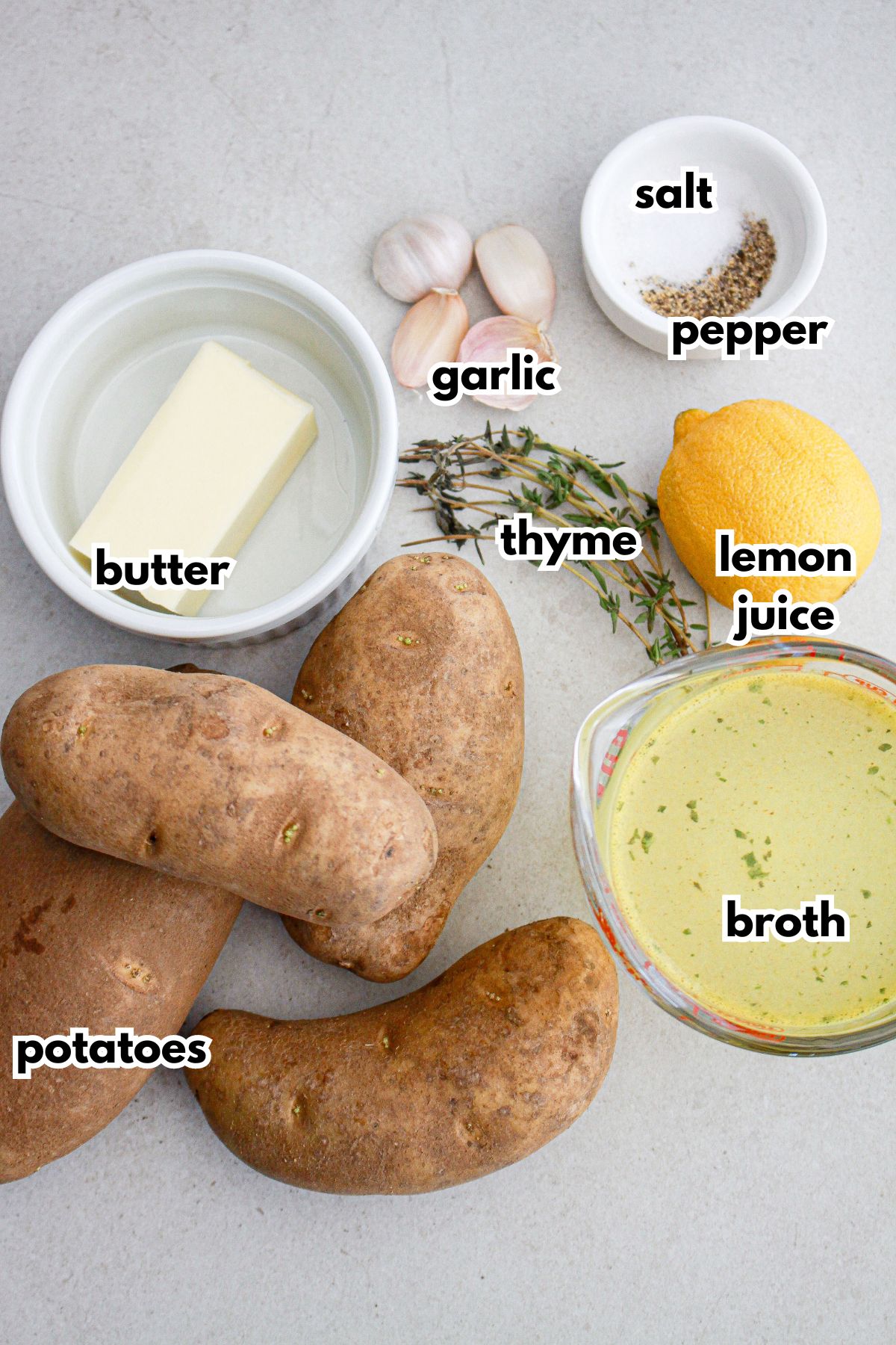 potatoes, butter, garlic, thyme, salt, pepper, lemon juice, and broth on a counter.