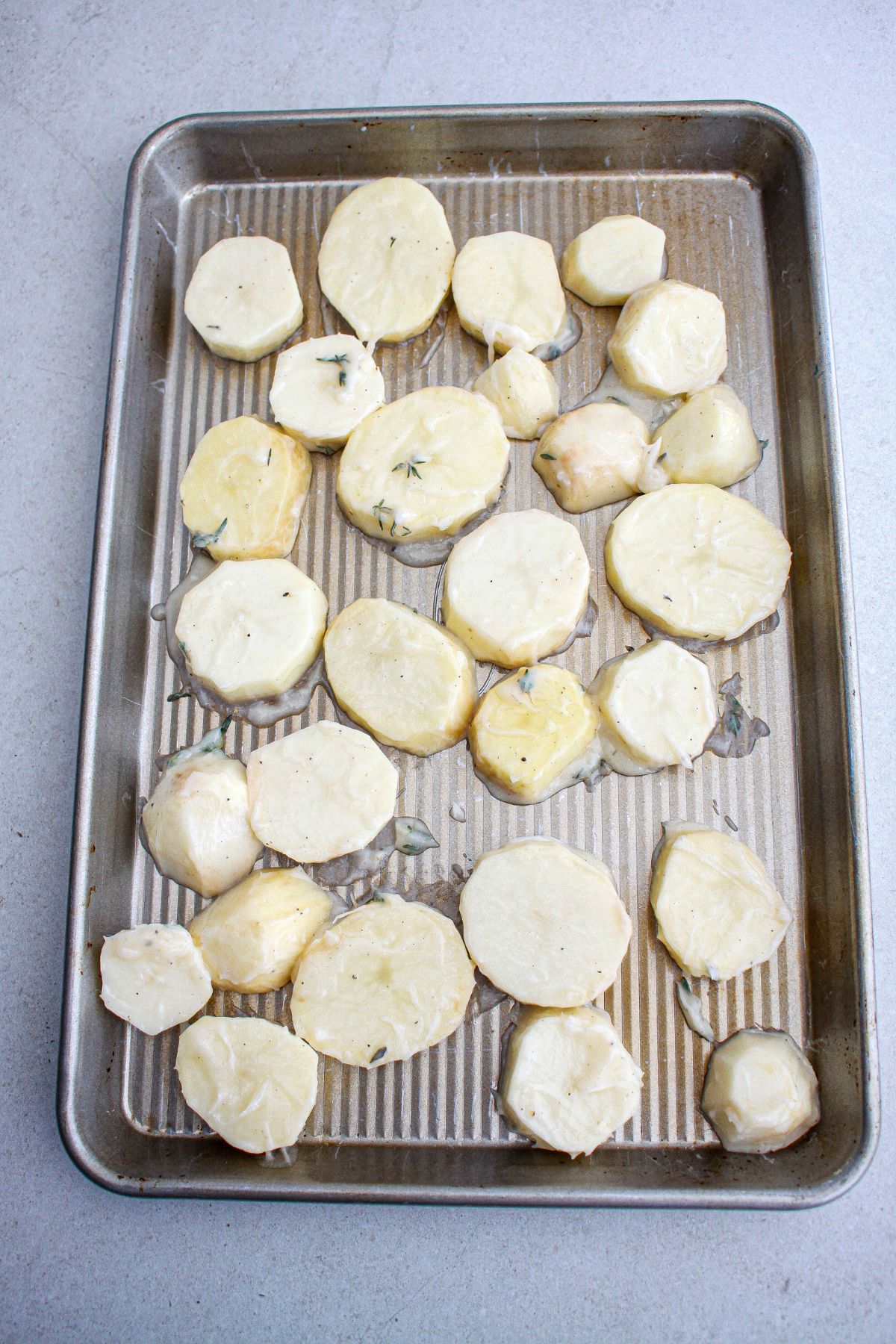 seasoned potatoes spread out on a baking sheet ready for the oven.