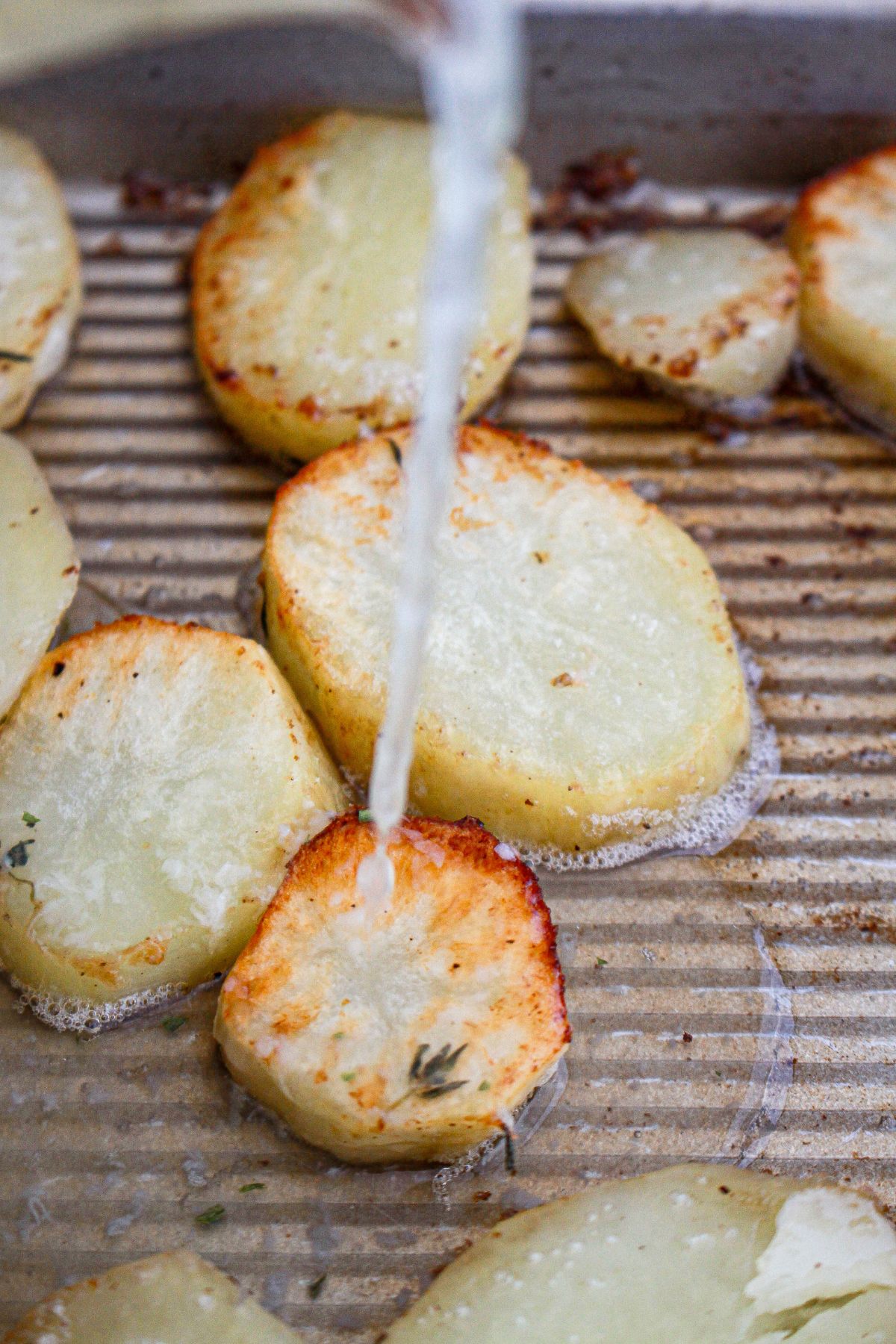 lemon and broth being poured over potatoes in a baking sheet.
