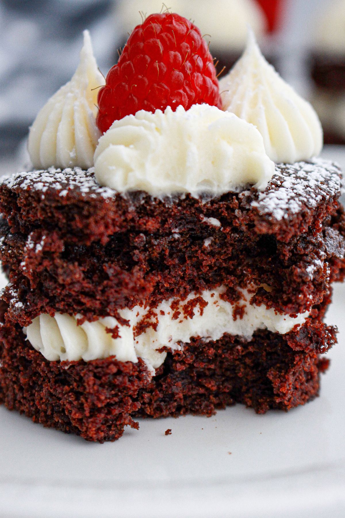 mini chocolate cake on a plate topped with a fresh raspberry with a bite missing from the cake.