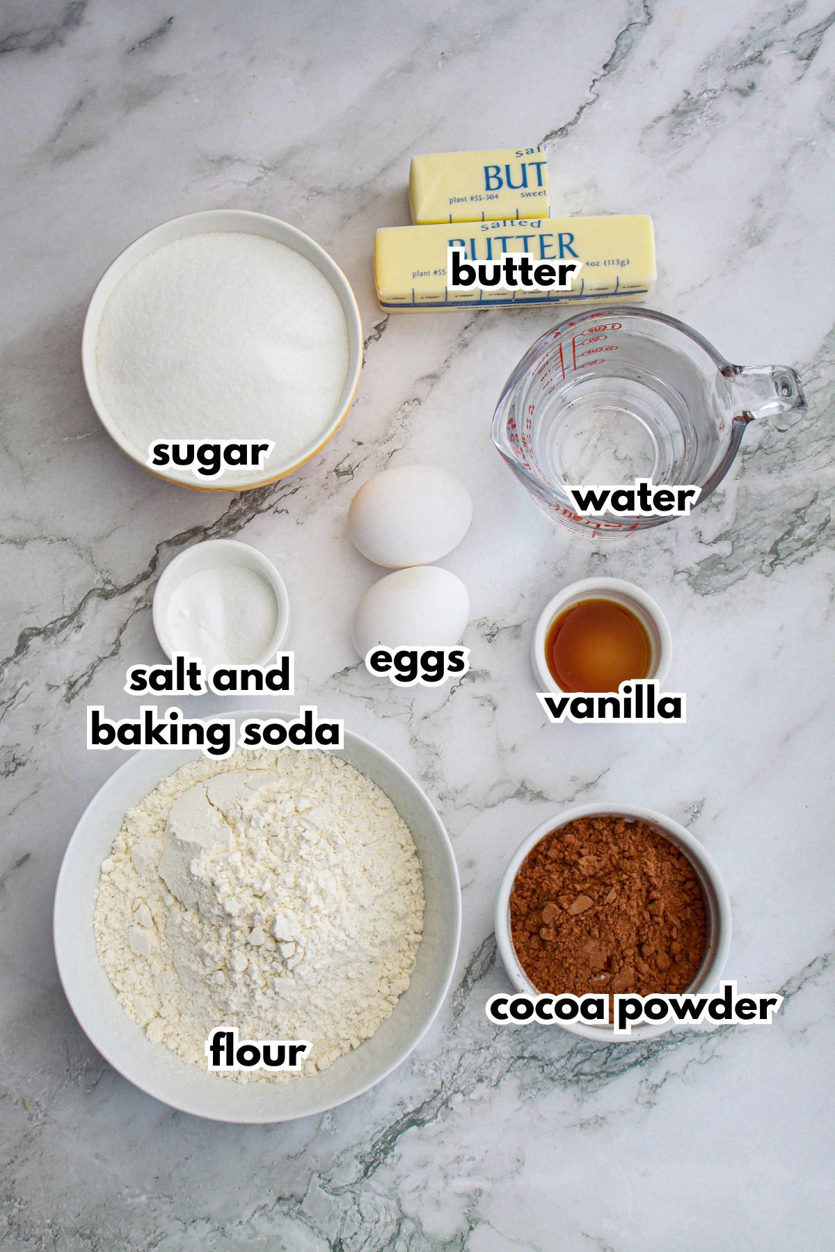bowls of butter, sugar, salt, baking soda, eggs, vanilla, flour, cocoa powder, and water on a counter.