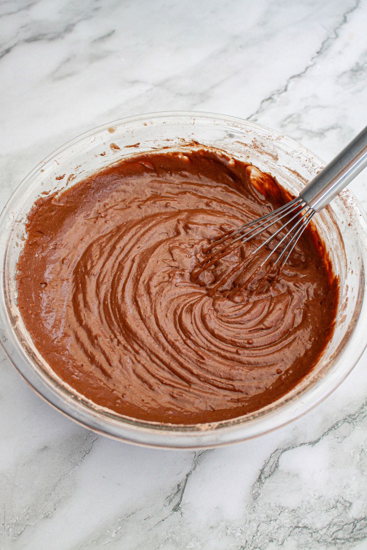 chocolate cake batter in a glass mixing being stirred with a whisk.