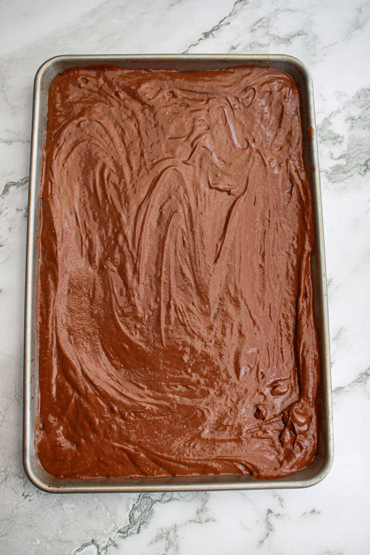chocolate cake batter spread into a sheet pan ready for the oven.