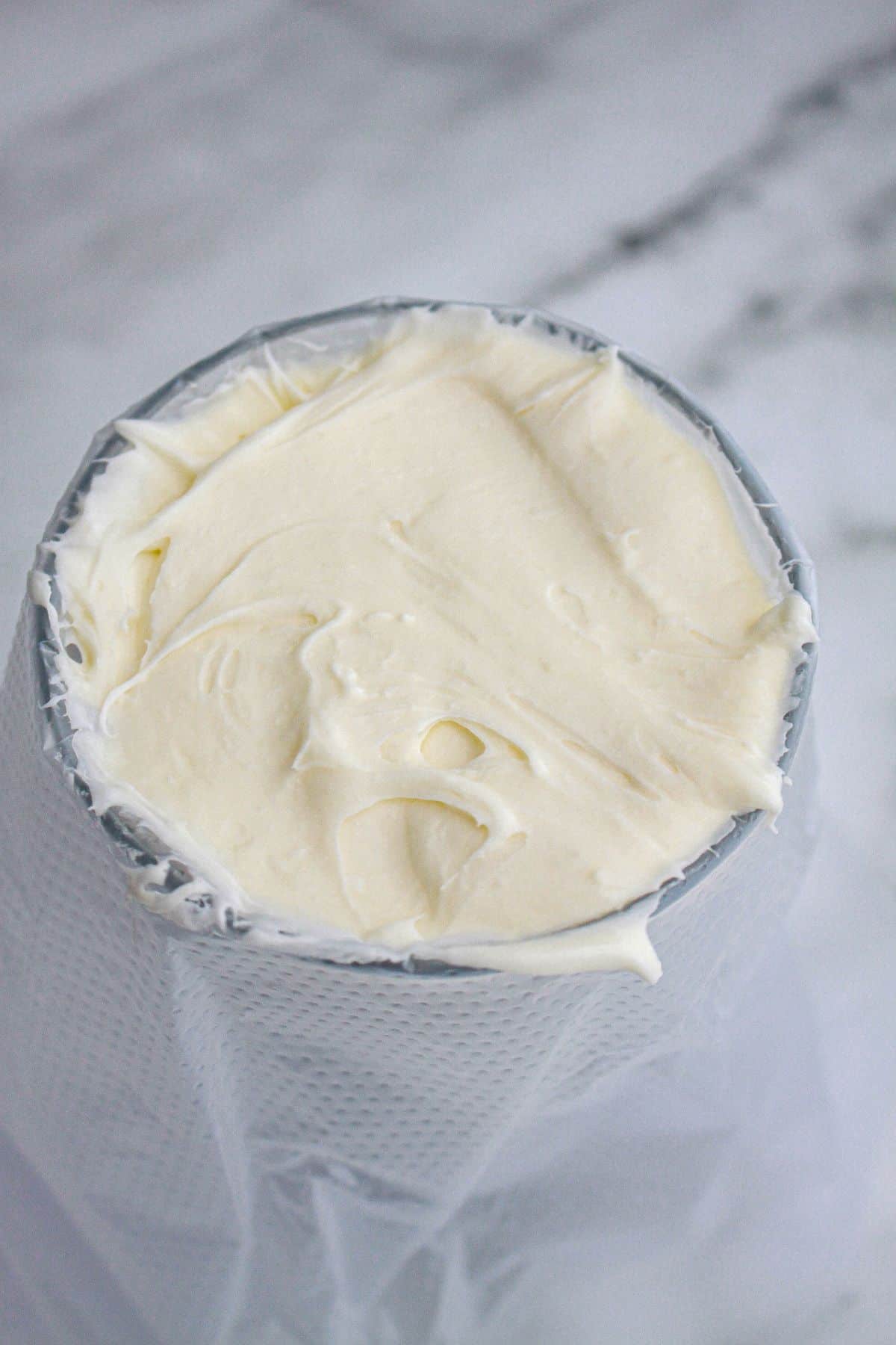 cream cheese frosting being added to a piping bag in a cup.