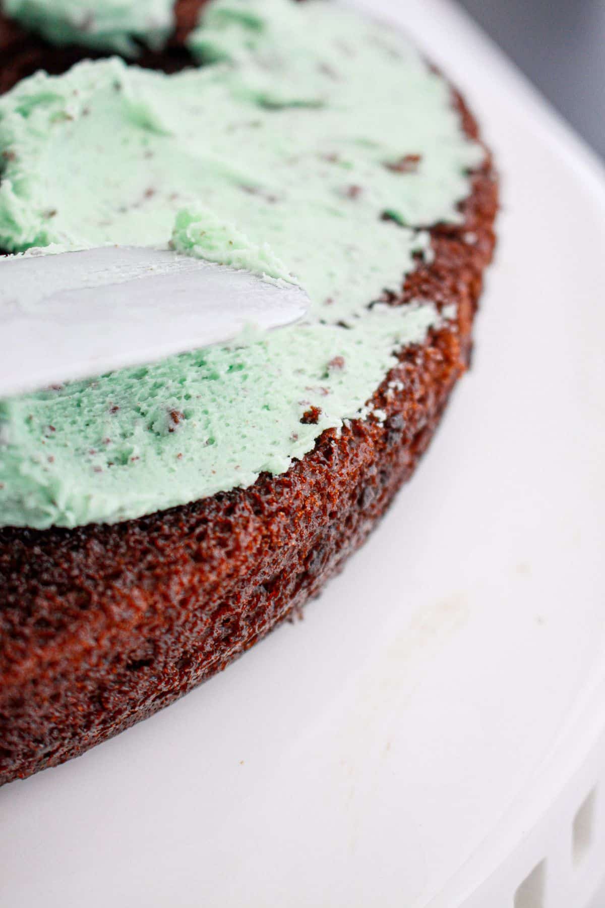 mint frosting being spread on top of a layer of chocolate cake.