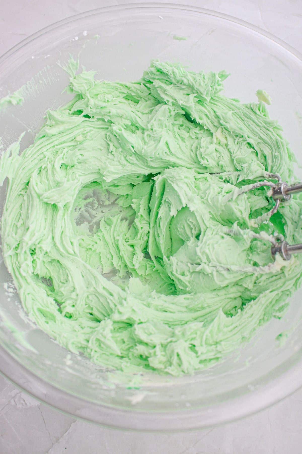 mint frosting being mixed with a hand mixer in a glass mixing bowl.