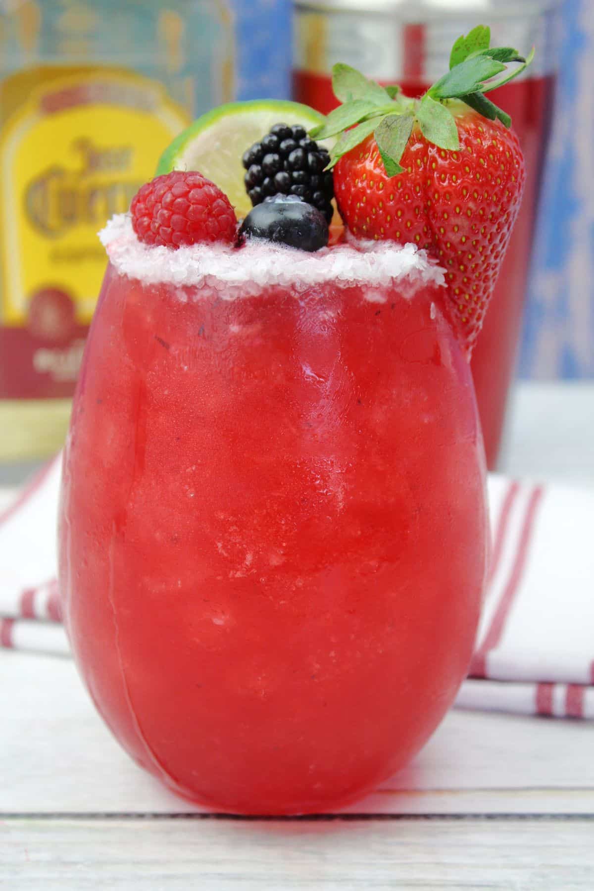 mixed berry cocktail garnished with a lime wedge, strawberry, blueberry, blackberry, and a raspberry.