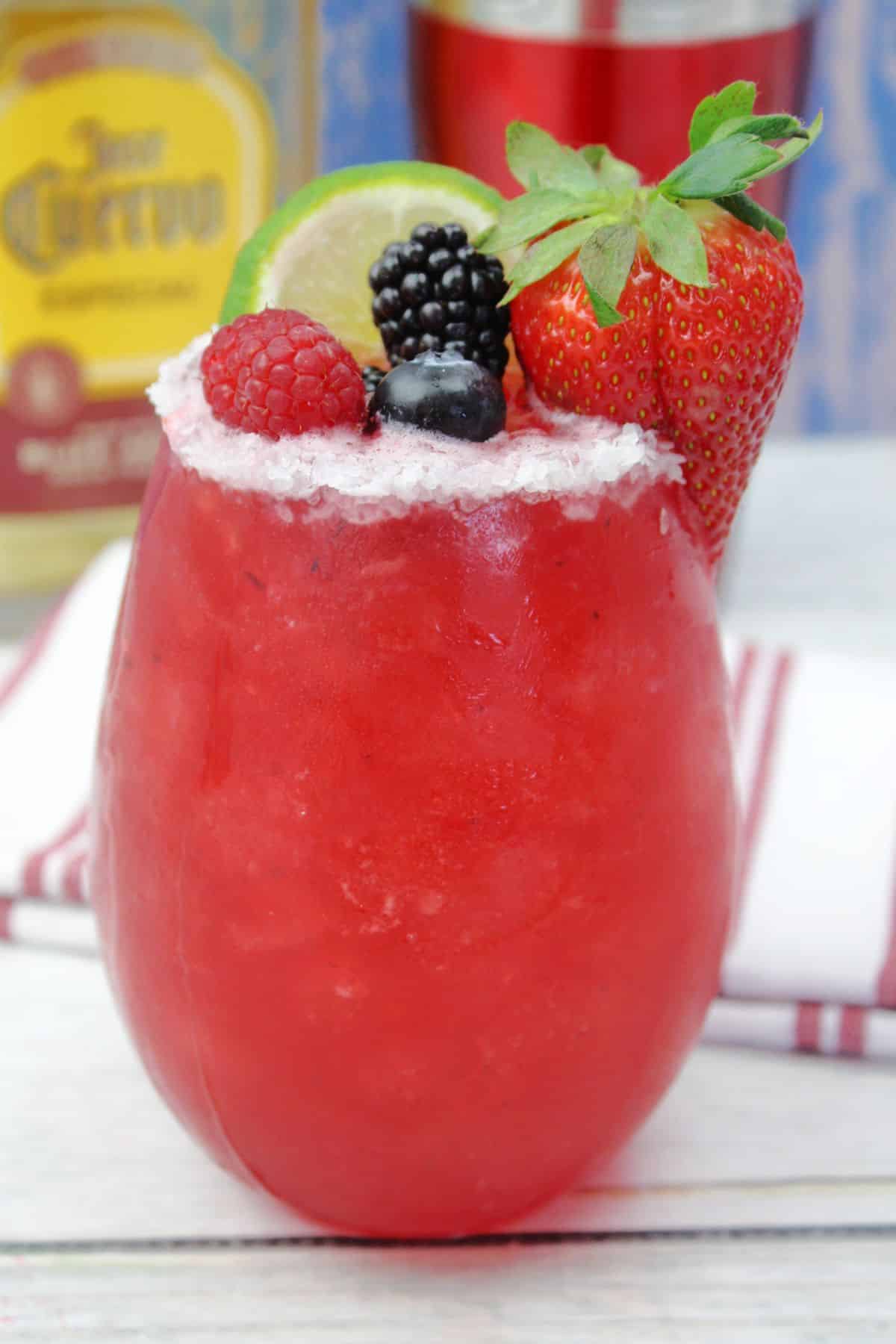 mixed berry cocktail garnished with a lime wedge, strawberry, blueberry, blackberry, and a raspberry.