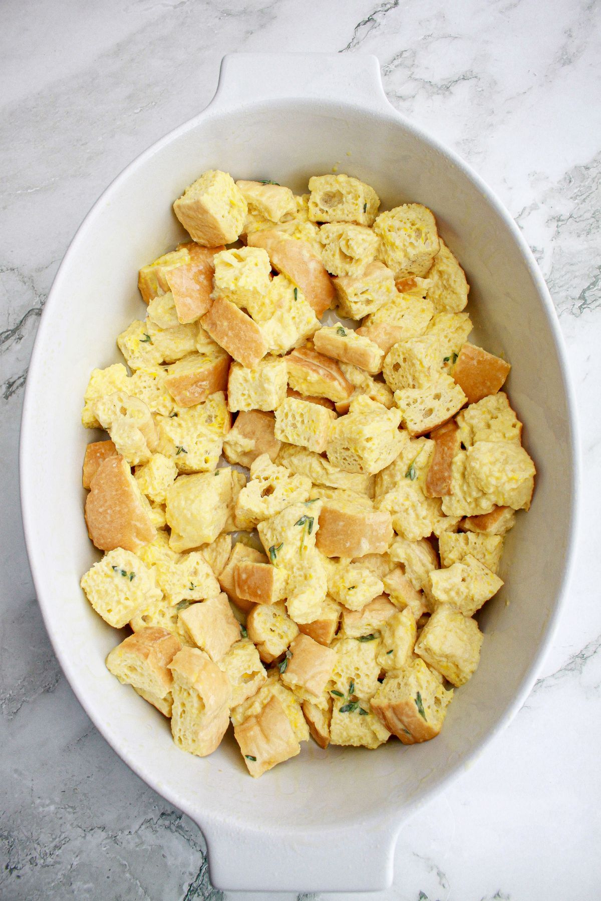 bread cubes being soaked in a baking dish.