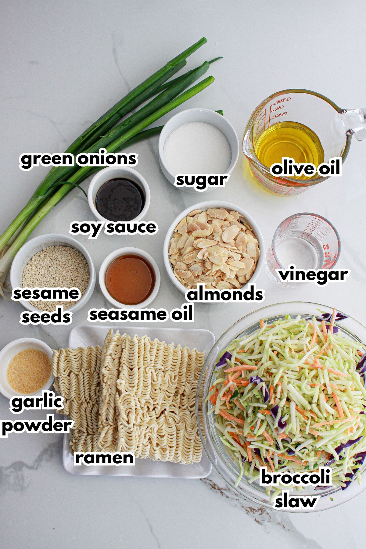bowls of green onions, sugar, soy sauce, sesame seeds, garlic powder, ramen, sesame oil, almonds, olive oil, vinegar, and broccoli slaw.