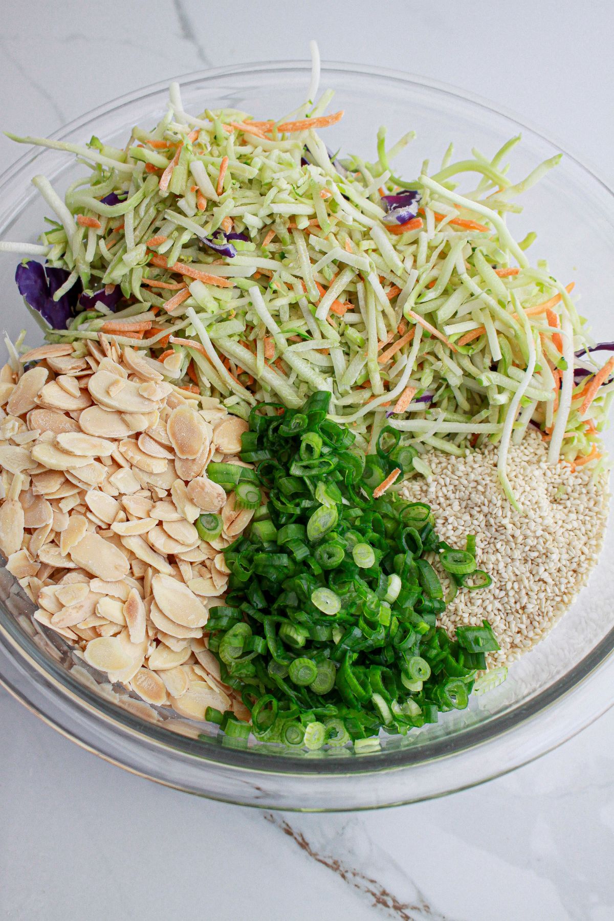 bowl of sesame seeds, broccoli slaw, sliced almonds, sliced green onions in a large bowl.