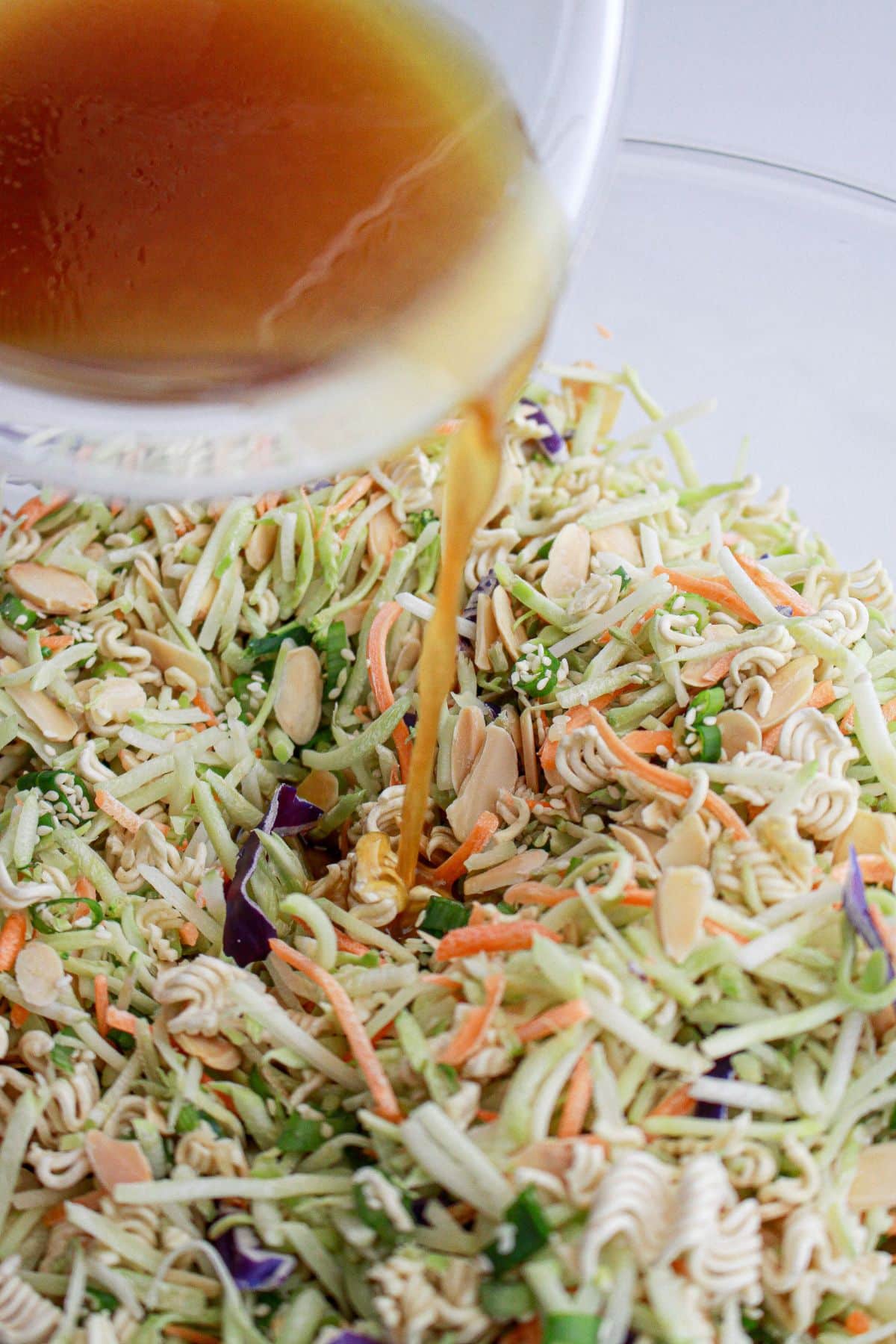 dressing being added on top of salad in a large bowl.