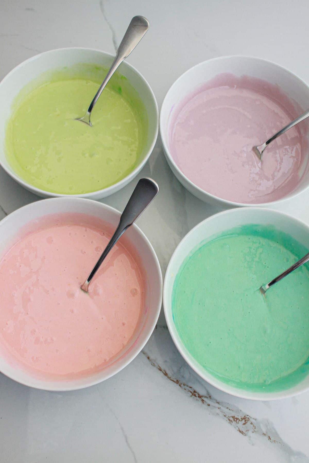 small bowls of yellow, pink, purple and green cake batter on a counter.