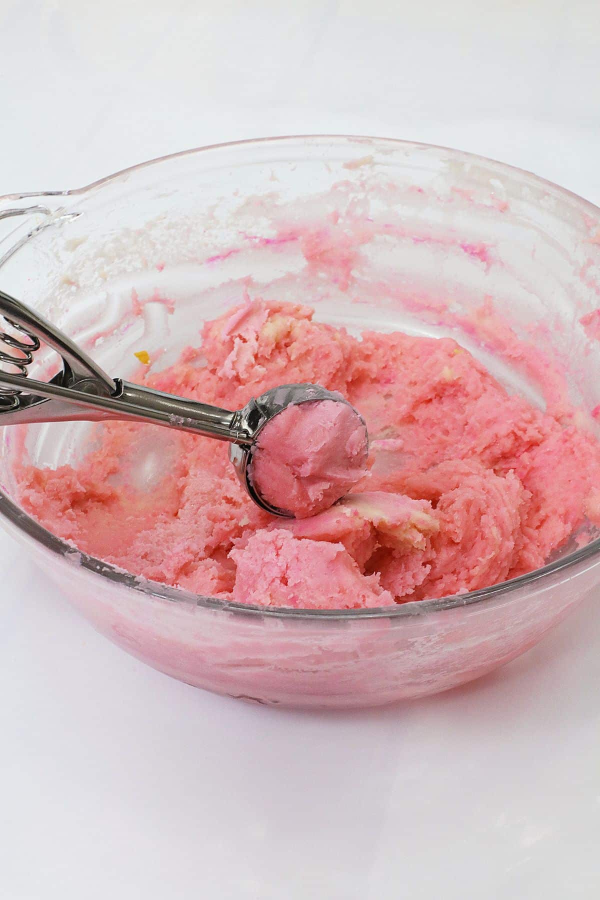 pink dough being scooped with an ice cream scoop.