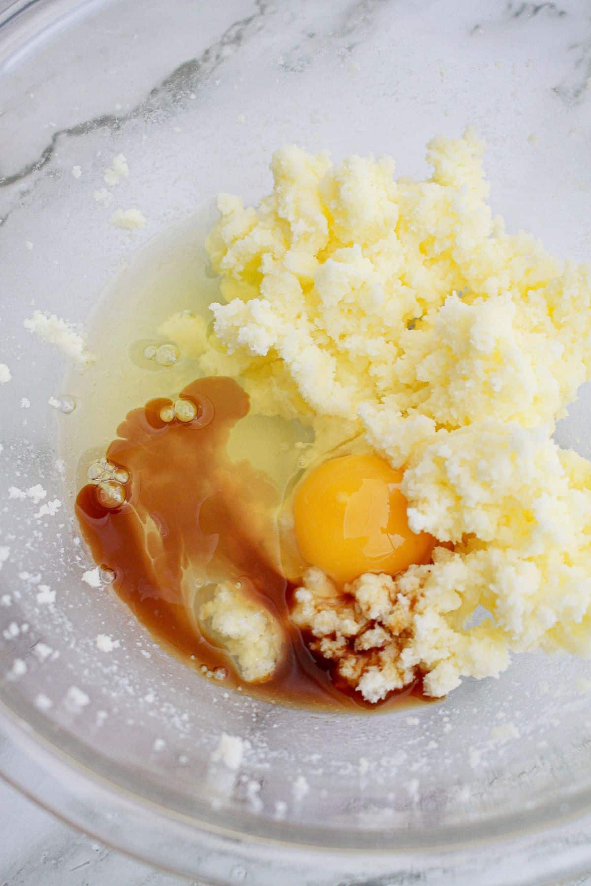 butter, sugar, eggs, and vanilla being mixed in a glass bowl.