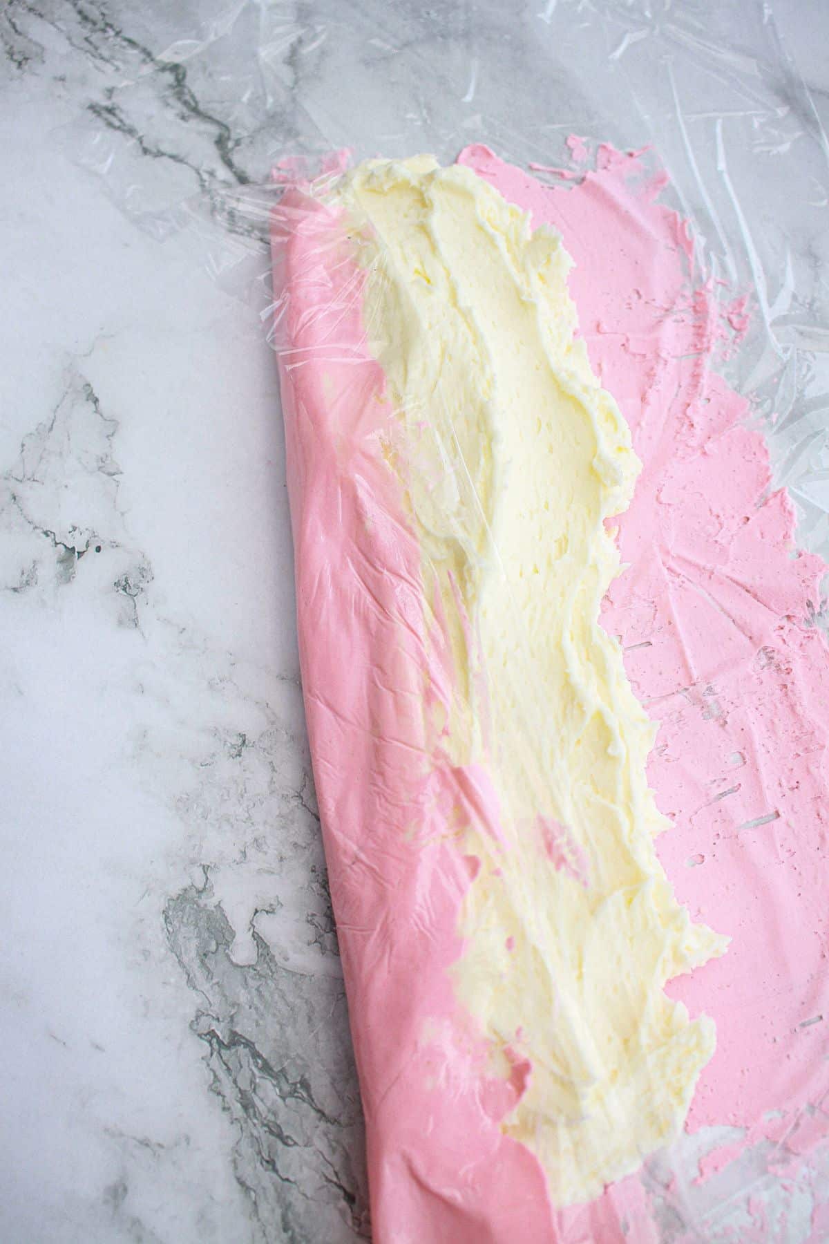 pink and white frosting being rolled in plastic wrap.