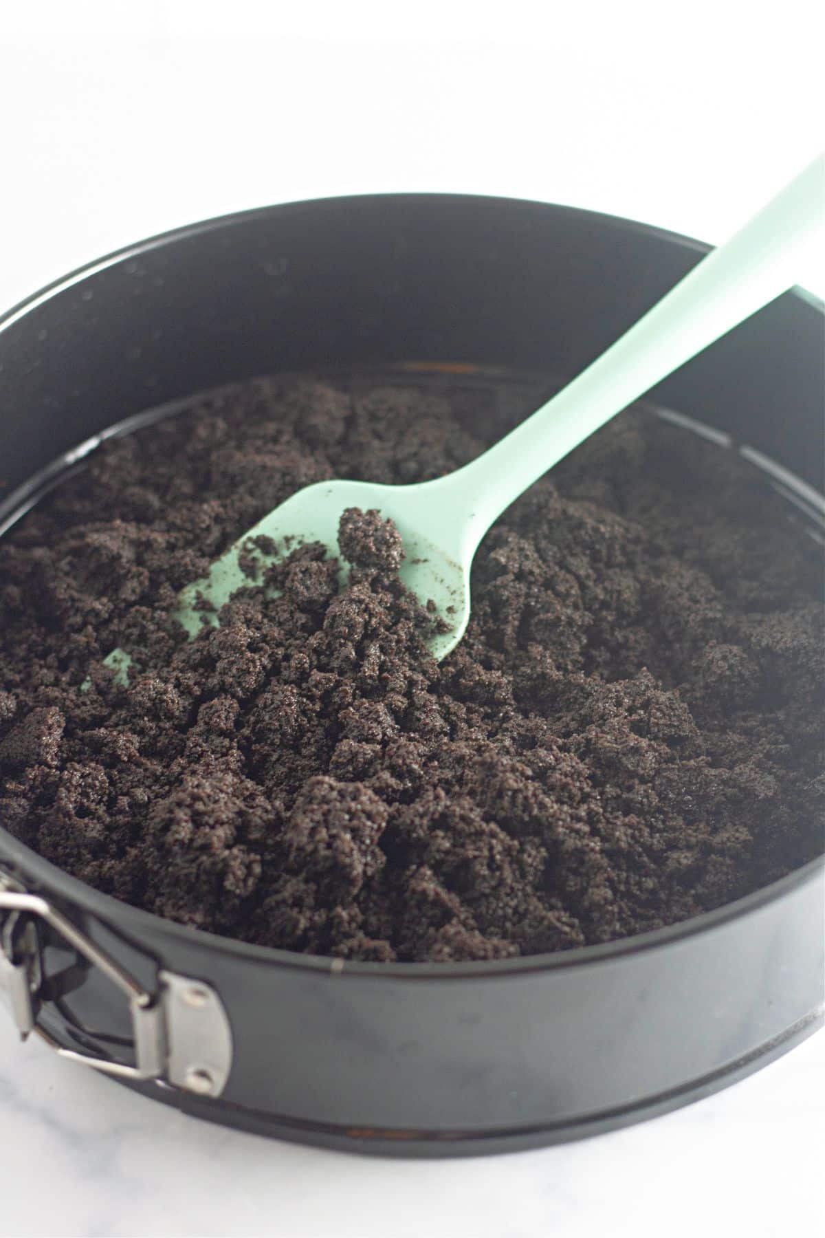 oreo crust being pressed into a springform pan.