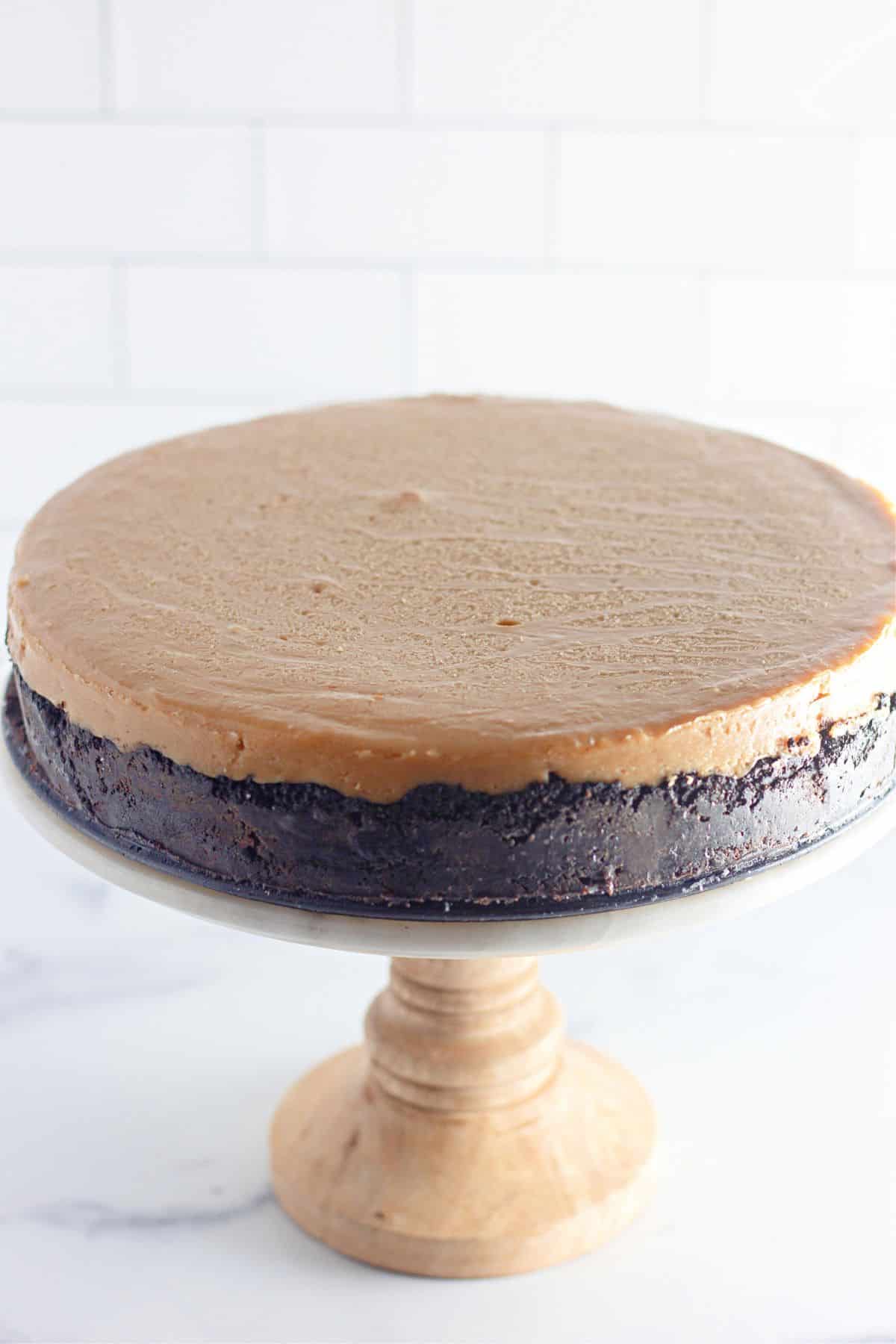 chocolate peanut butter cheesecake cooling on a cake stand.