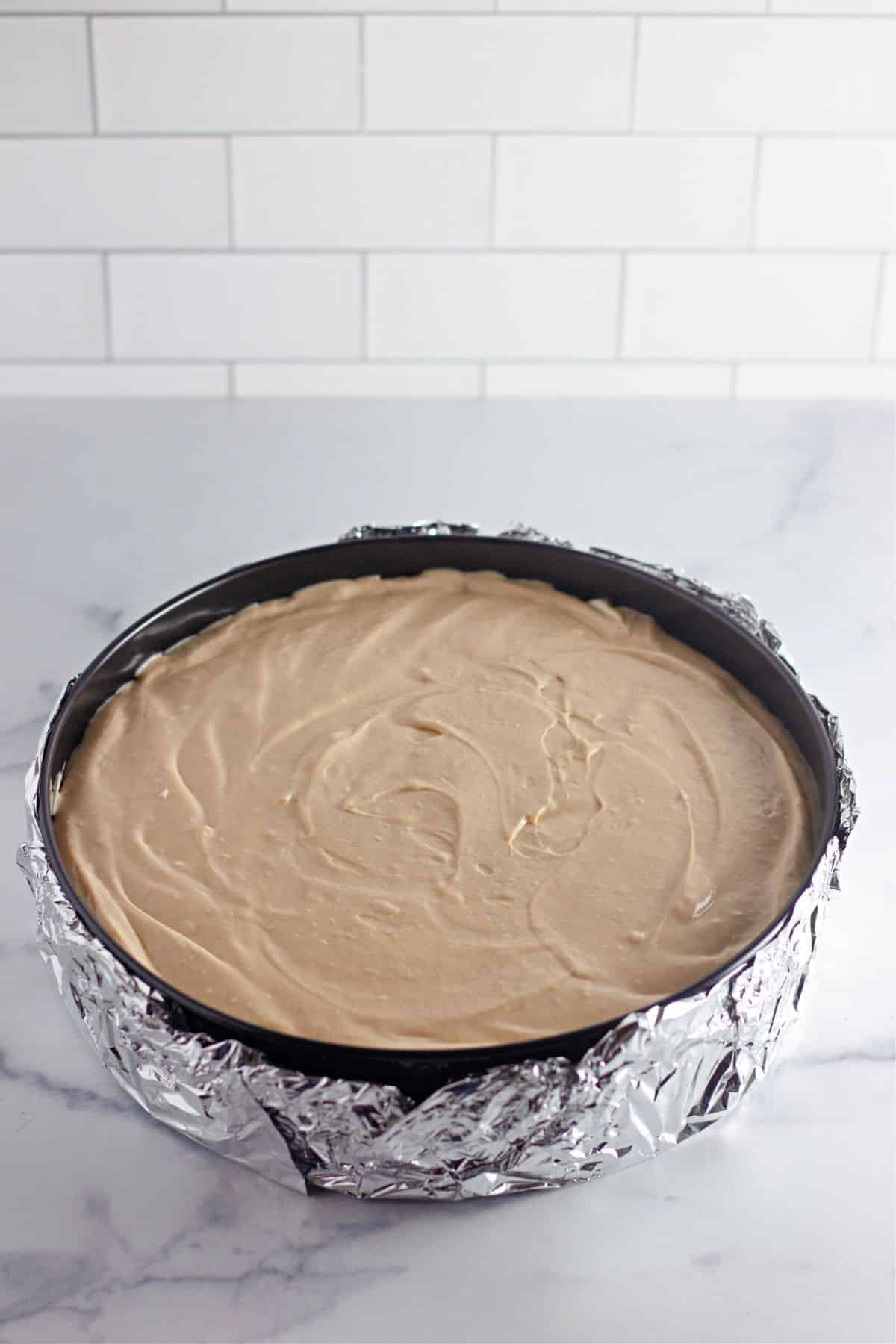 cheesecake batter being added to a springform pan with foil on the bottom.