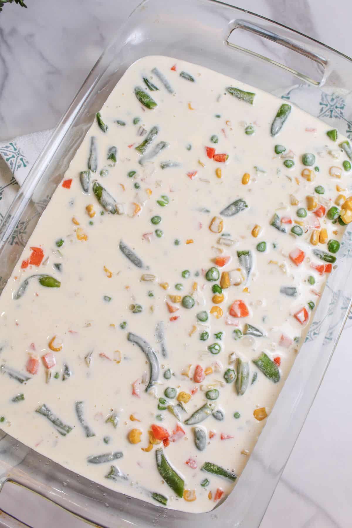 cream sauce being added to a baking dish filled with vegetables.