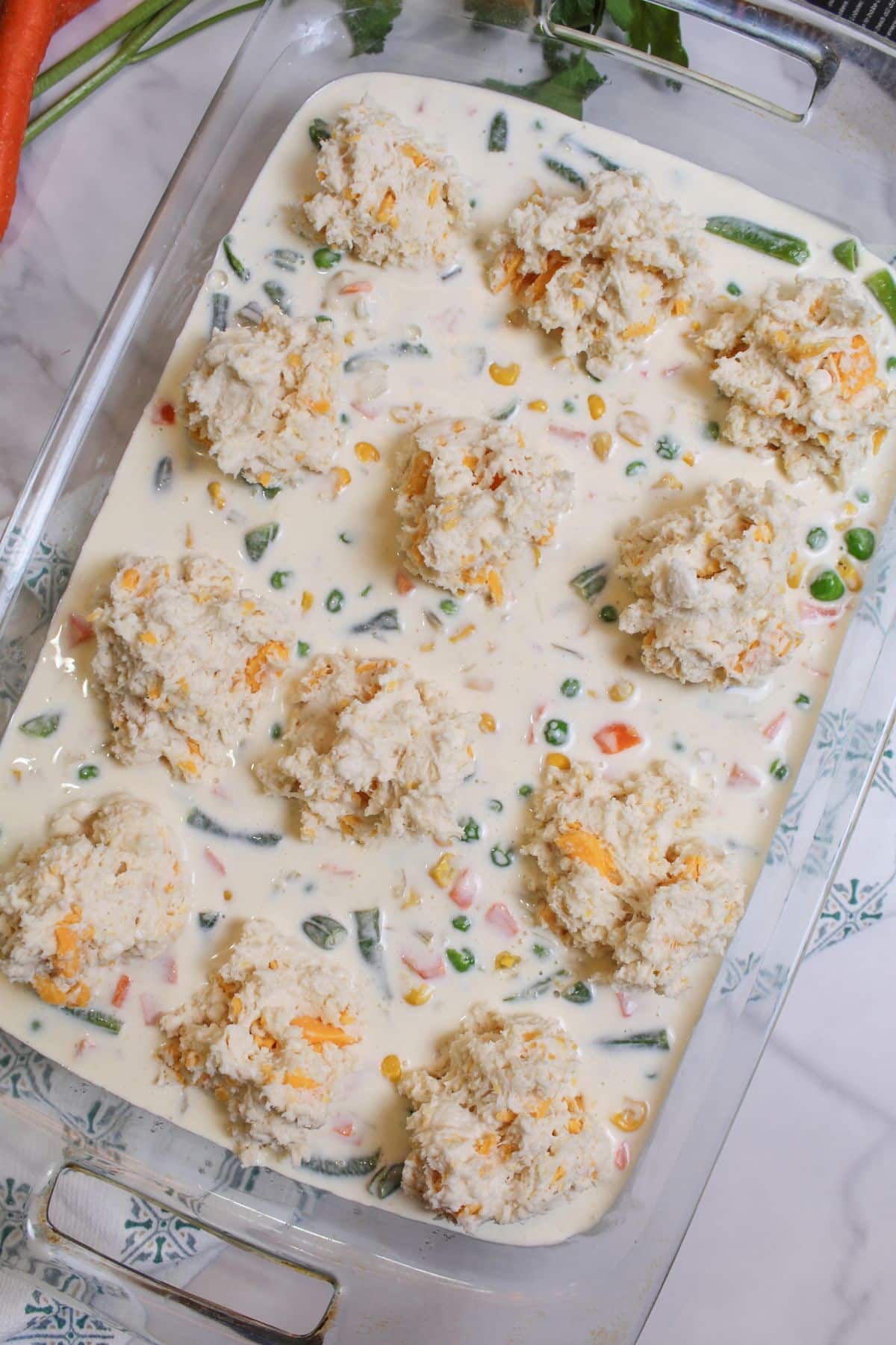 biscuit mix being added to the top of seafood casserole in a glass baking dish.