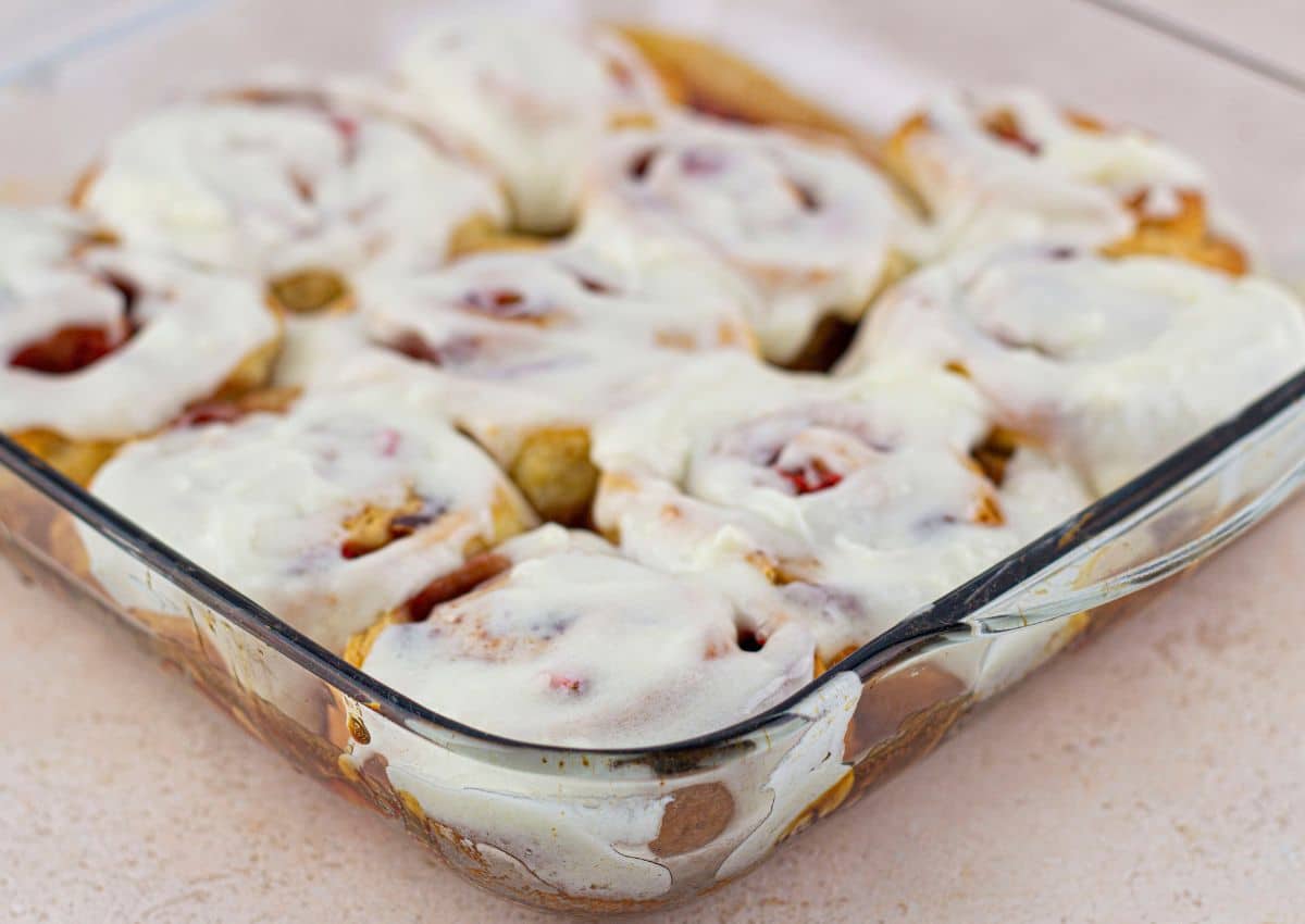 glaze being added no top of cinnamon rolls in a baking dish.