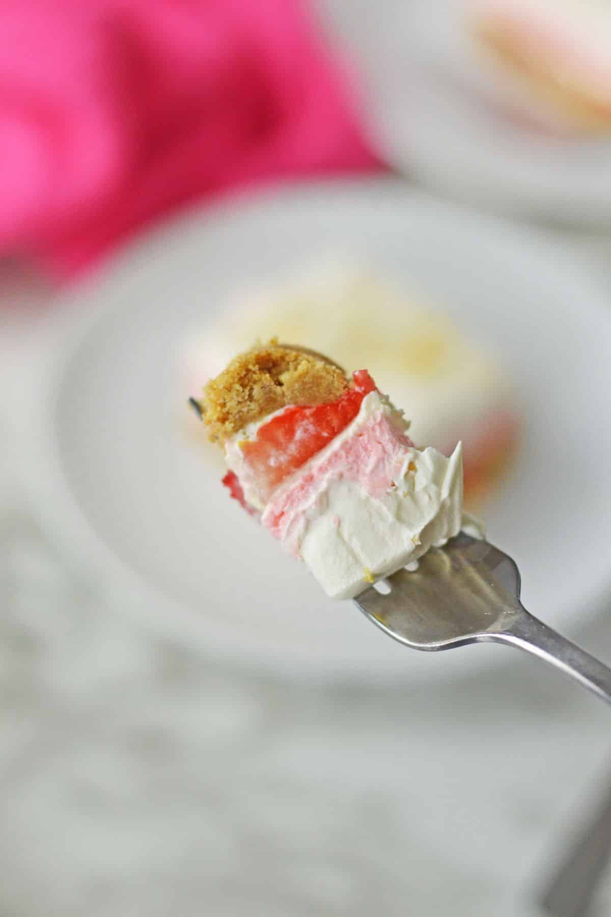 bite of no bake strawberry delight on a fork held in the air.