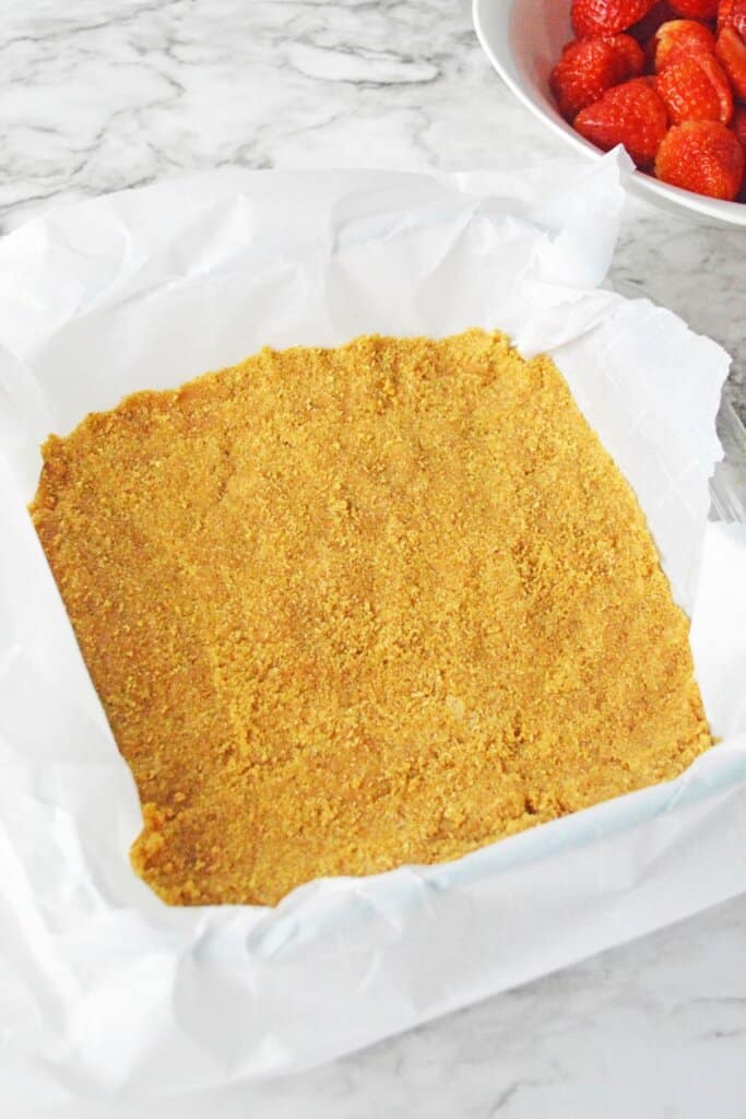 graham cracker crust being pressed into a parchment lined baking sheet.