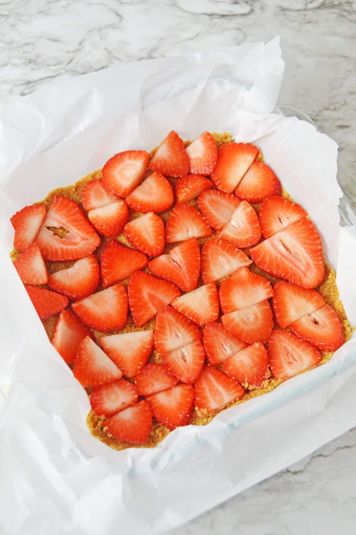 sliced strawberries being layered on top of a crust in a parchment lined baking sheet.