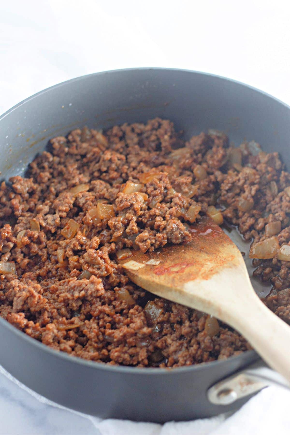 taco seasoning being added to ground beef and onions in a large skillet.
