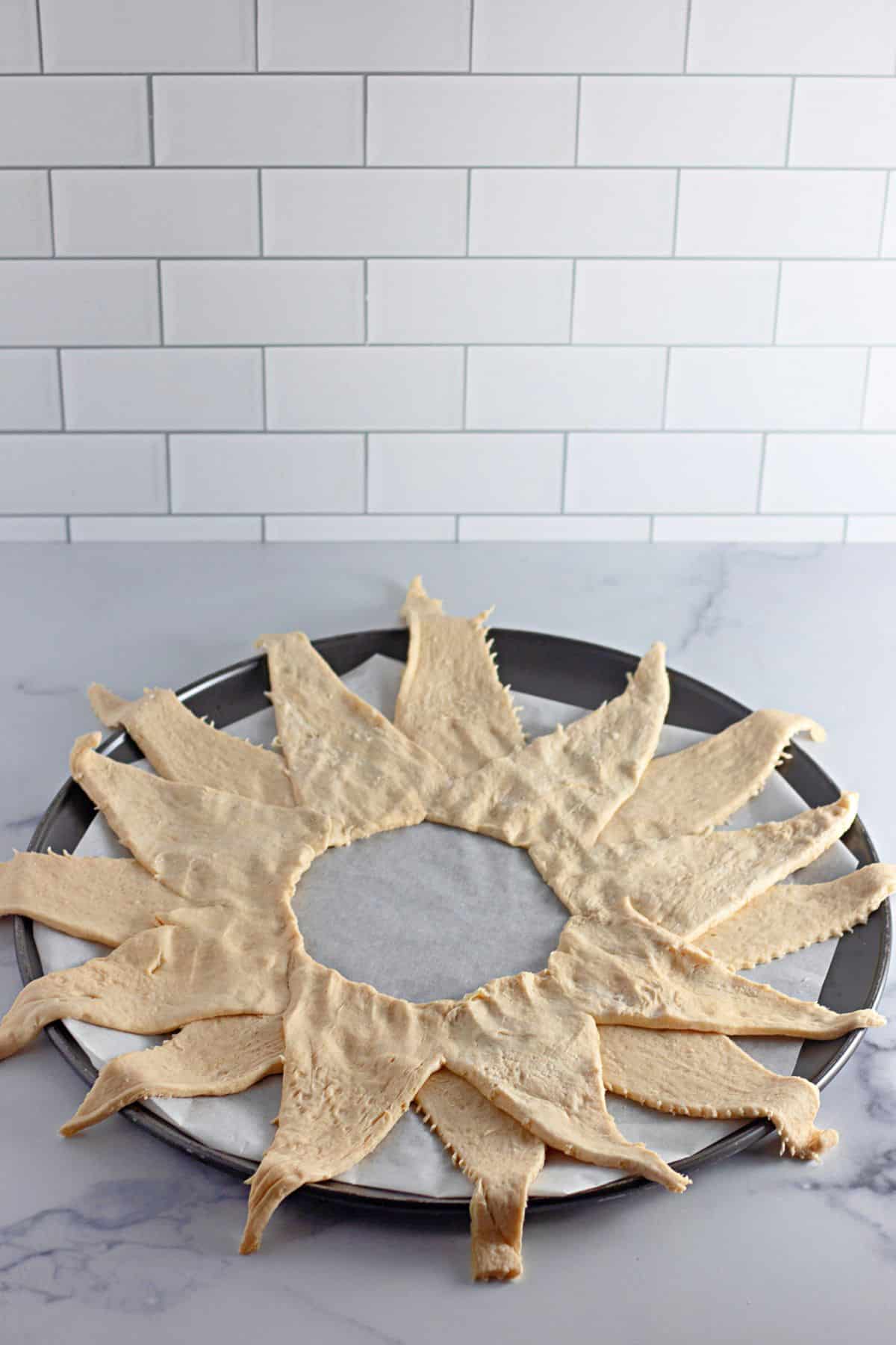 crescents rolls laid out on a parchment lined baking pan in a sun shape.