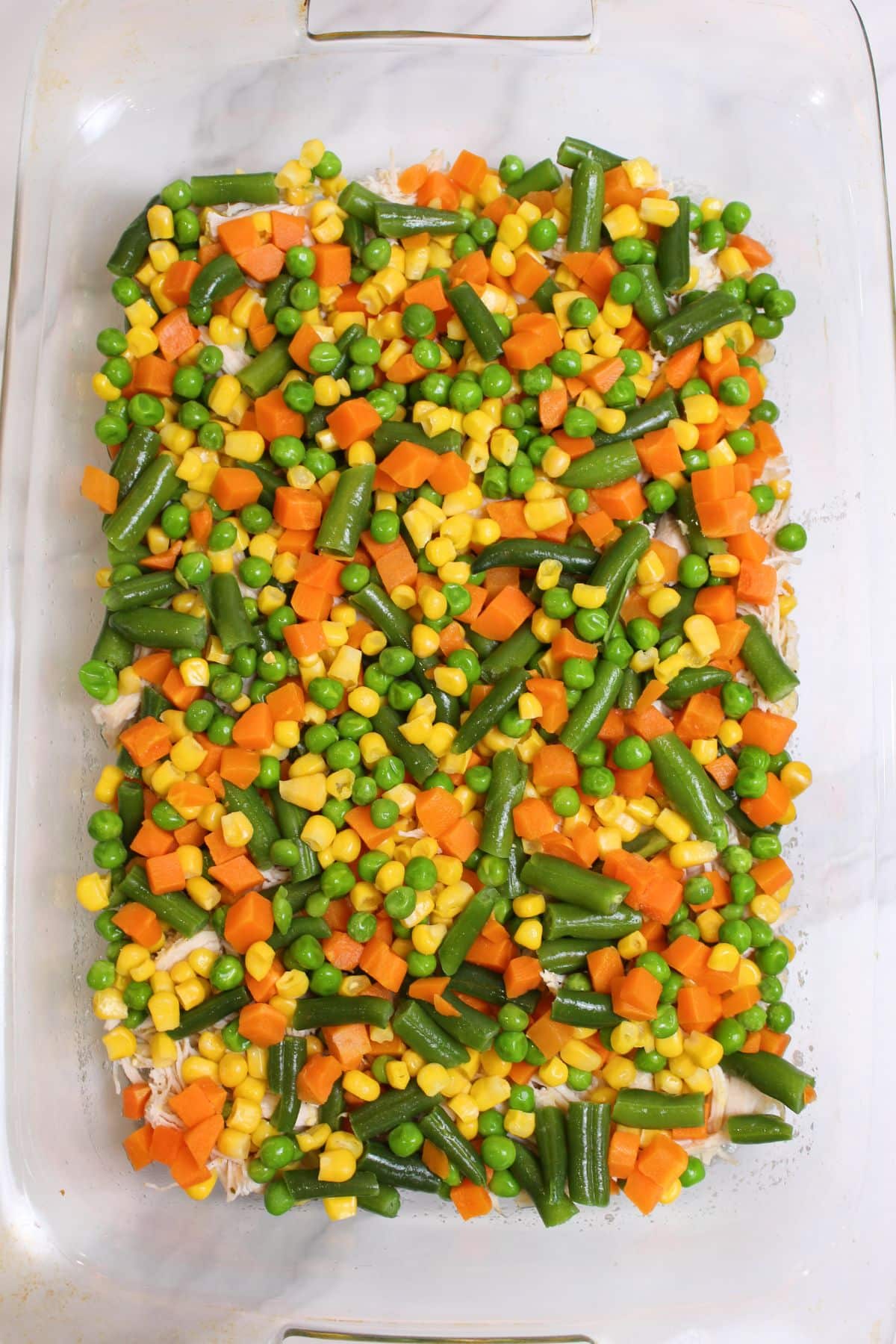 shredded chicken and frozen mixed vegetables in a glass casserole dish.