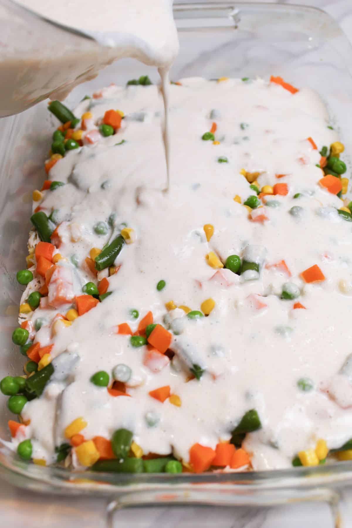 biscuit mix being poured over top of vegetables in a casserole dish.
