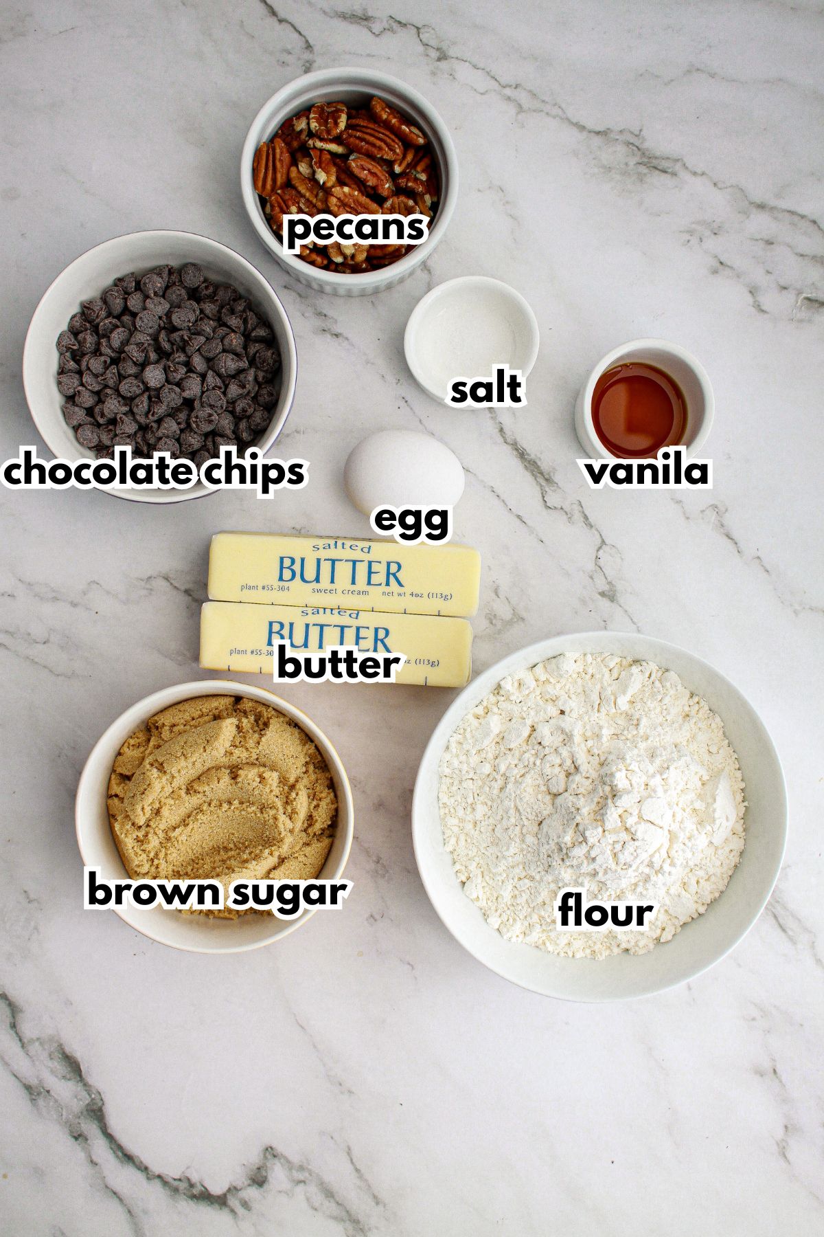 bowls of pecans, chocolate chips, salt, egg, vanilla extract, butter, brown sugar, and flour.